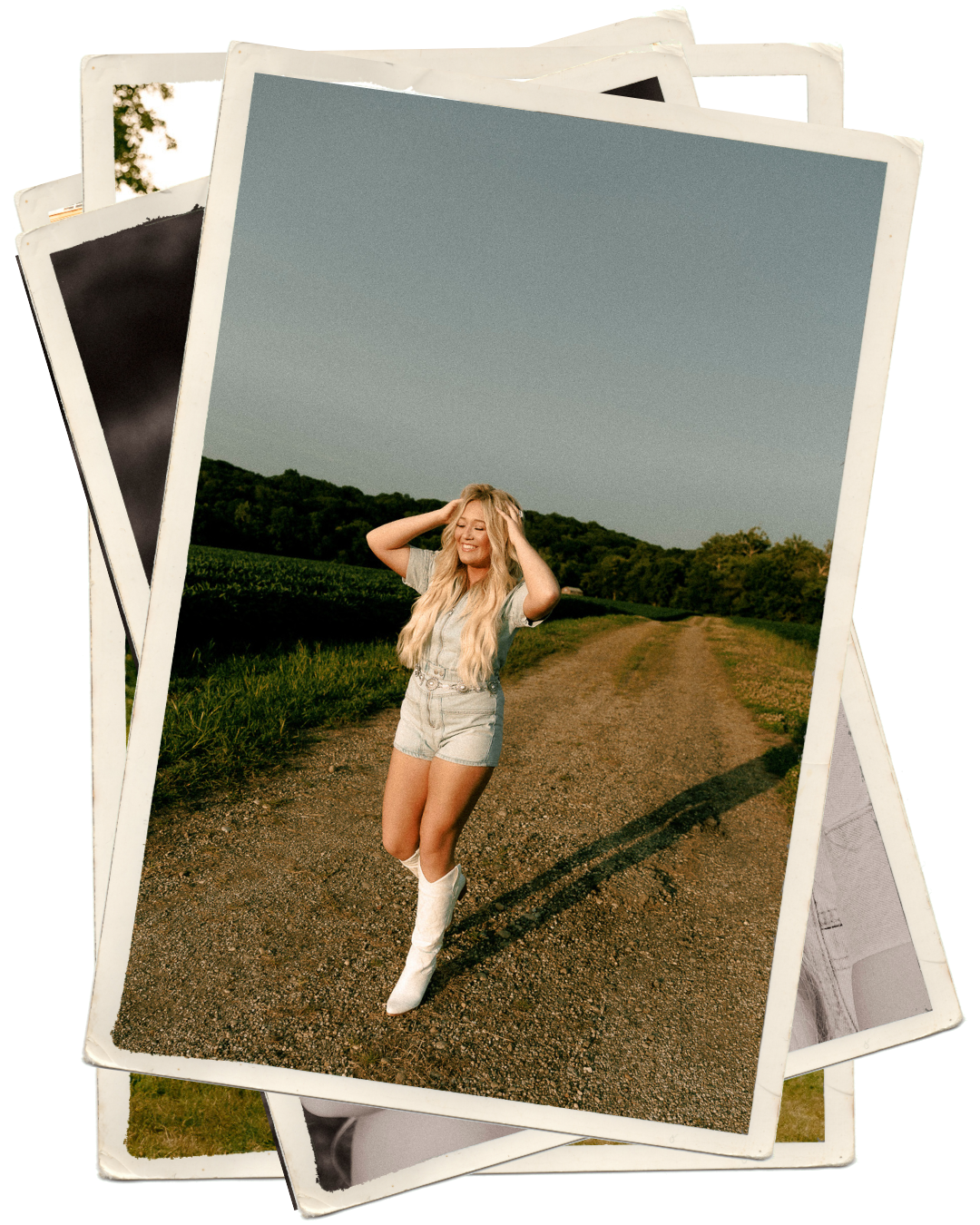 Blonde woman in denim shorts and white boots poses on a rural dirt road surrounded by green fields.