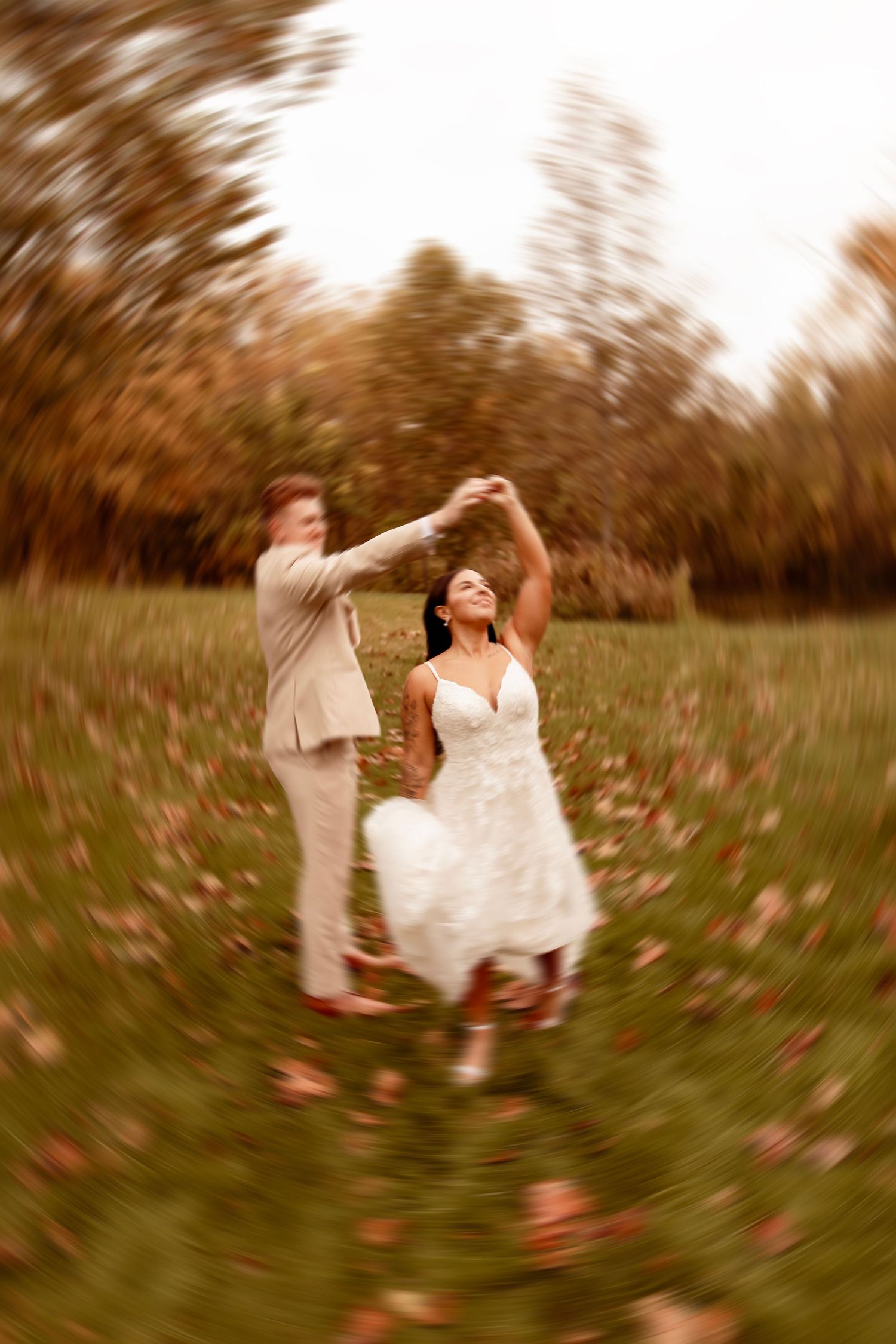 A couple dances together in a field of autumn leaves with a dreamy, motion-blurred effect.