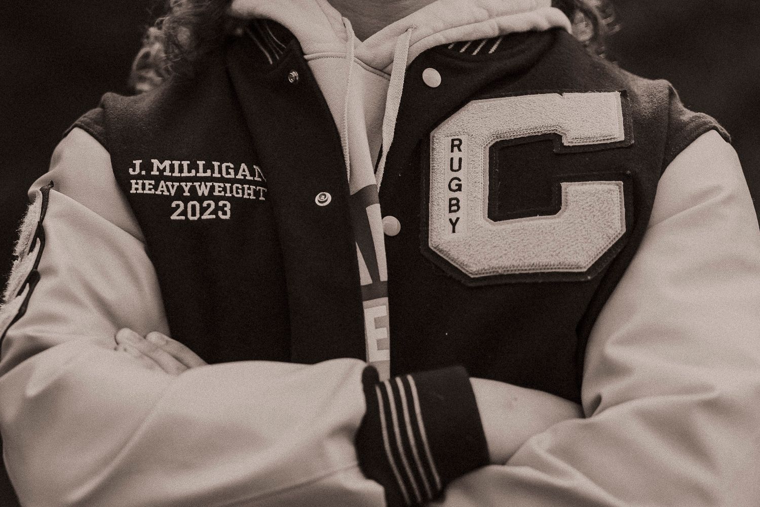 Black and white photo of a varsity letterman jacket with rugby patch, reading J. Milligan Heavyweight 2023.