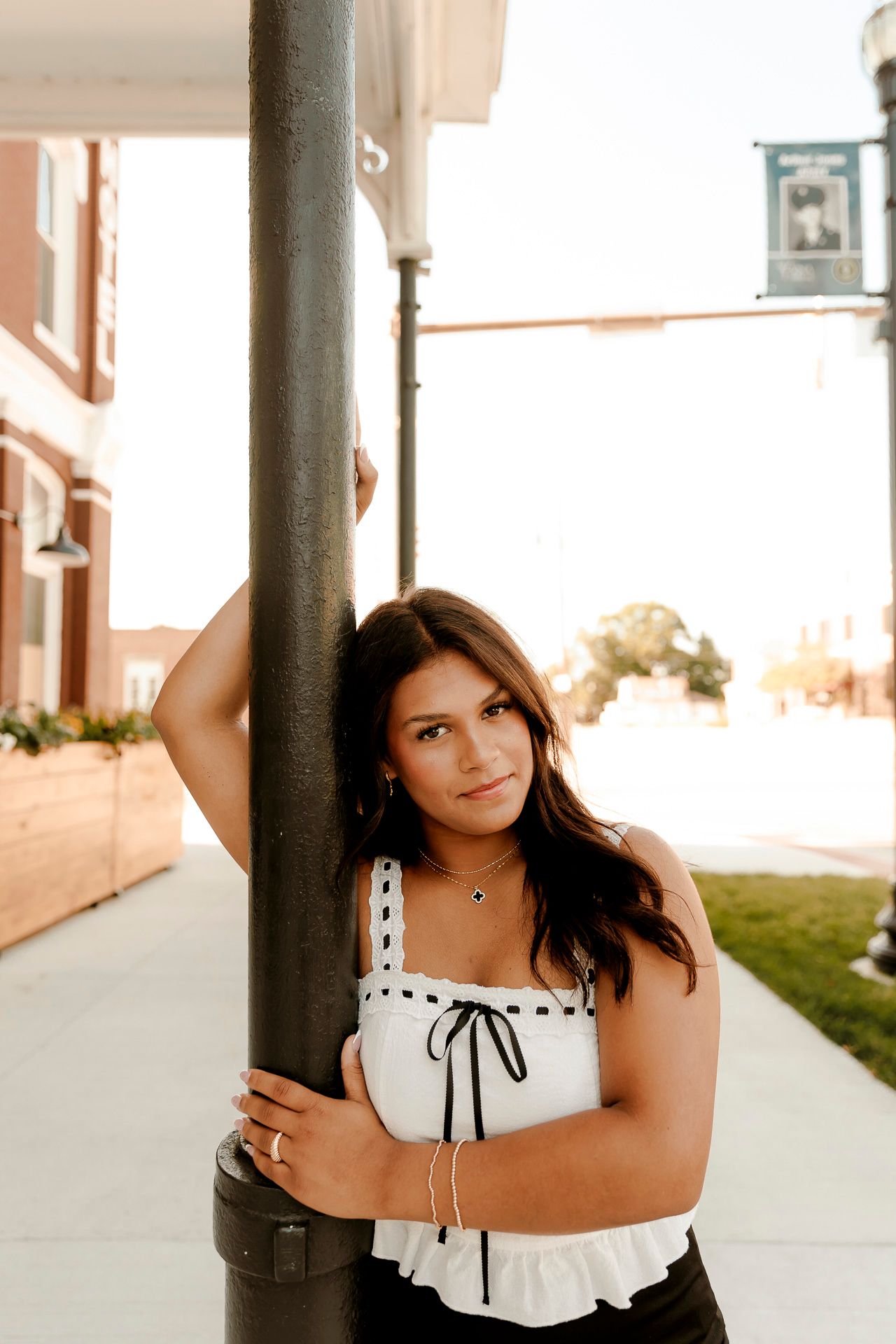 Young woman in white top leaning against a street pole in an urban setting during golden hour.