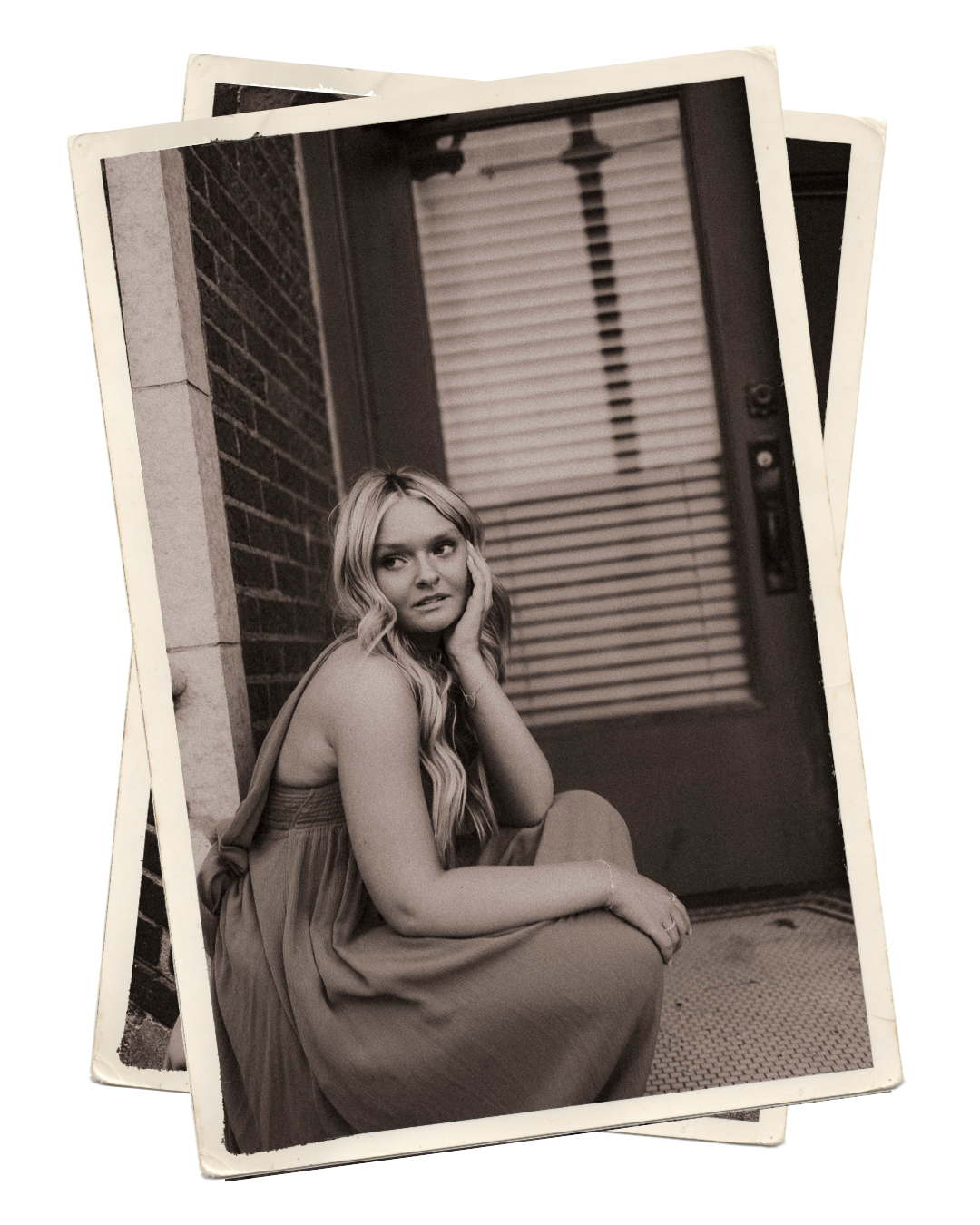 Vintage sepia-toned photo of a blonde woman in a flowing dress sitting on steps against a brick wall.
