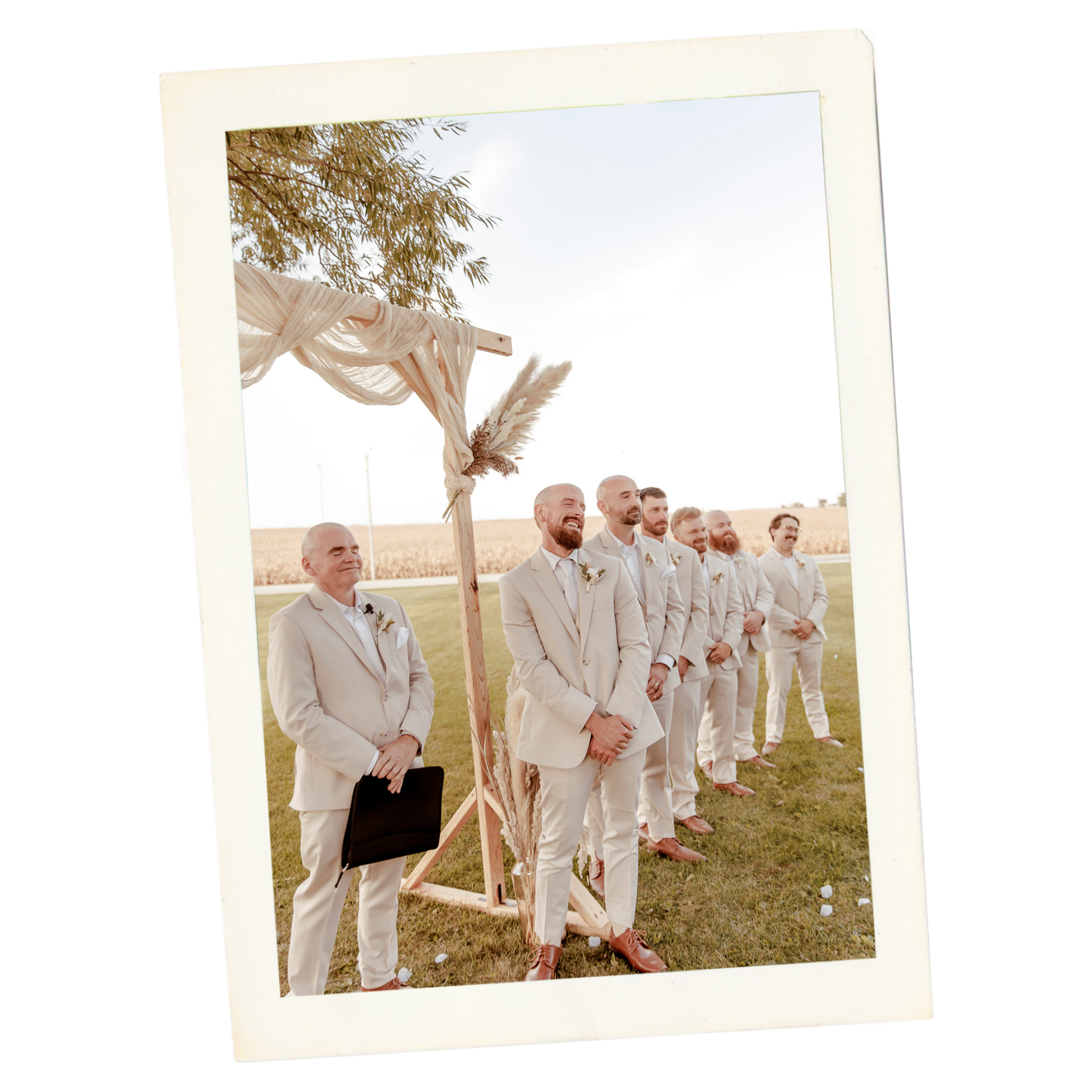 Wedding party in light colored suits stands in a line outdoors during a sunny celebration.