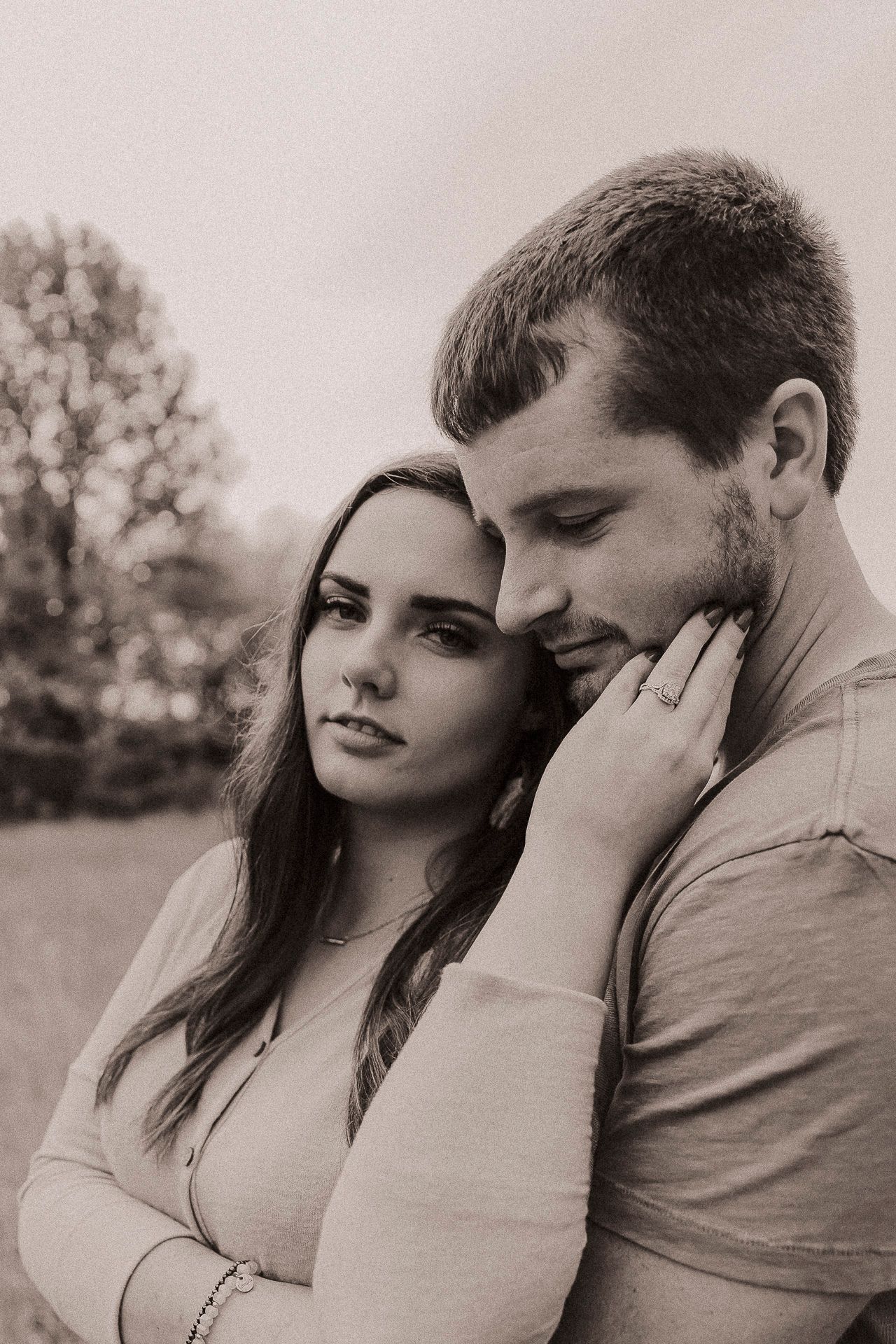 Black and white portrait of a couple embracing outdoors, woman resting her hand on man's face.