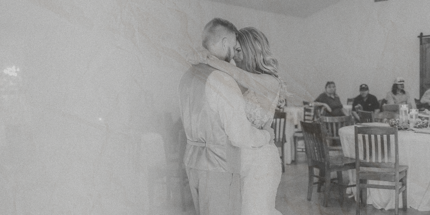 Two people embrace in a black and white photo while others sit at tables in the background.