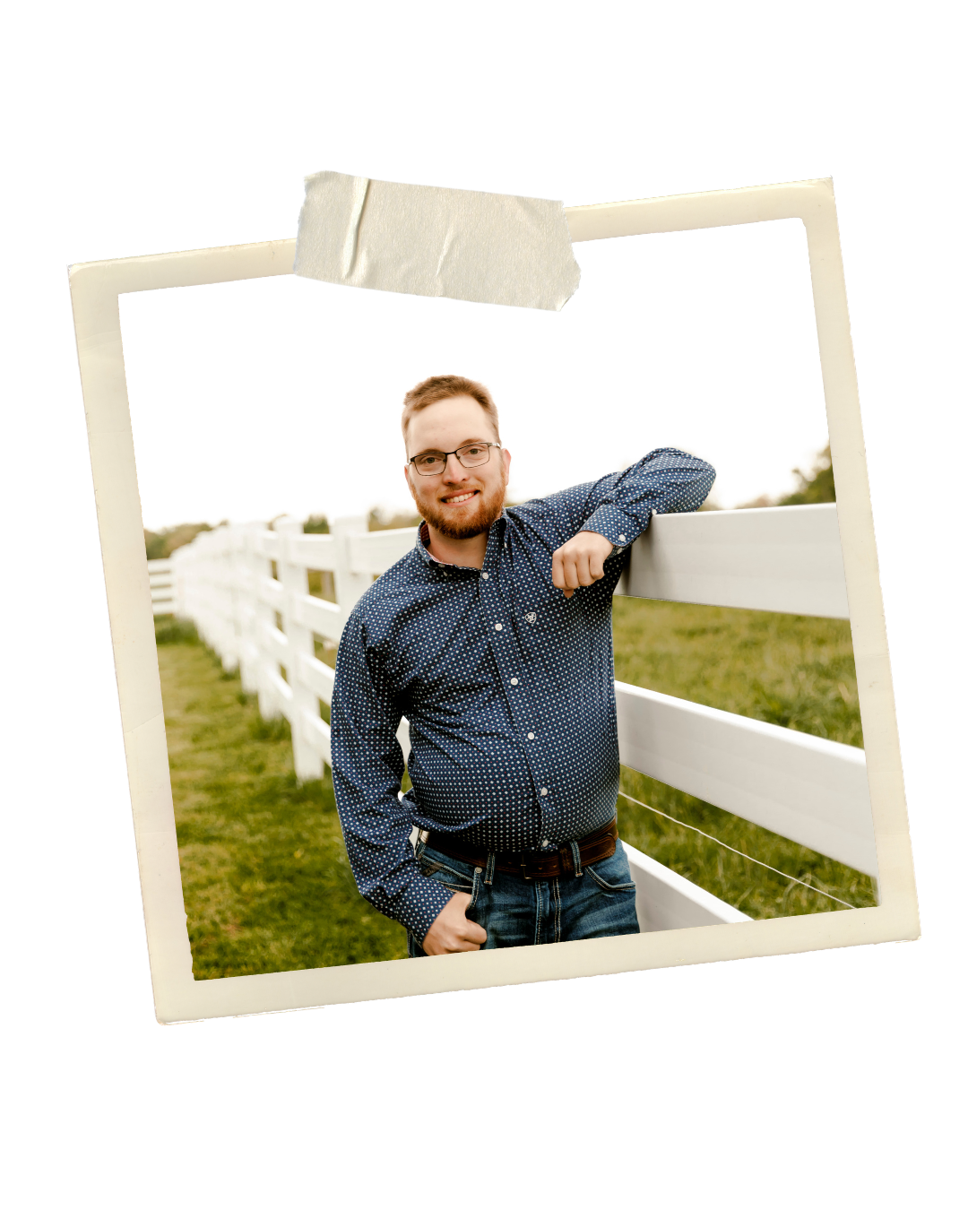 Smiling bearded man in a blue patterned shirt leaning on a white wooden fence in a rural farm setting.