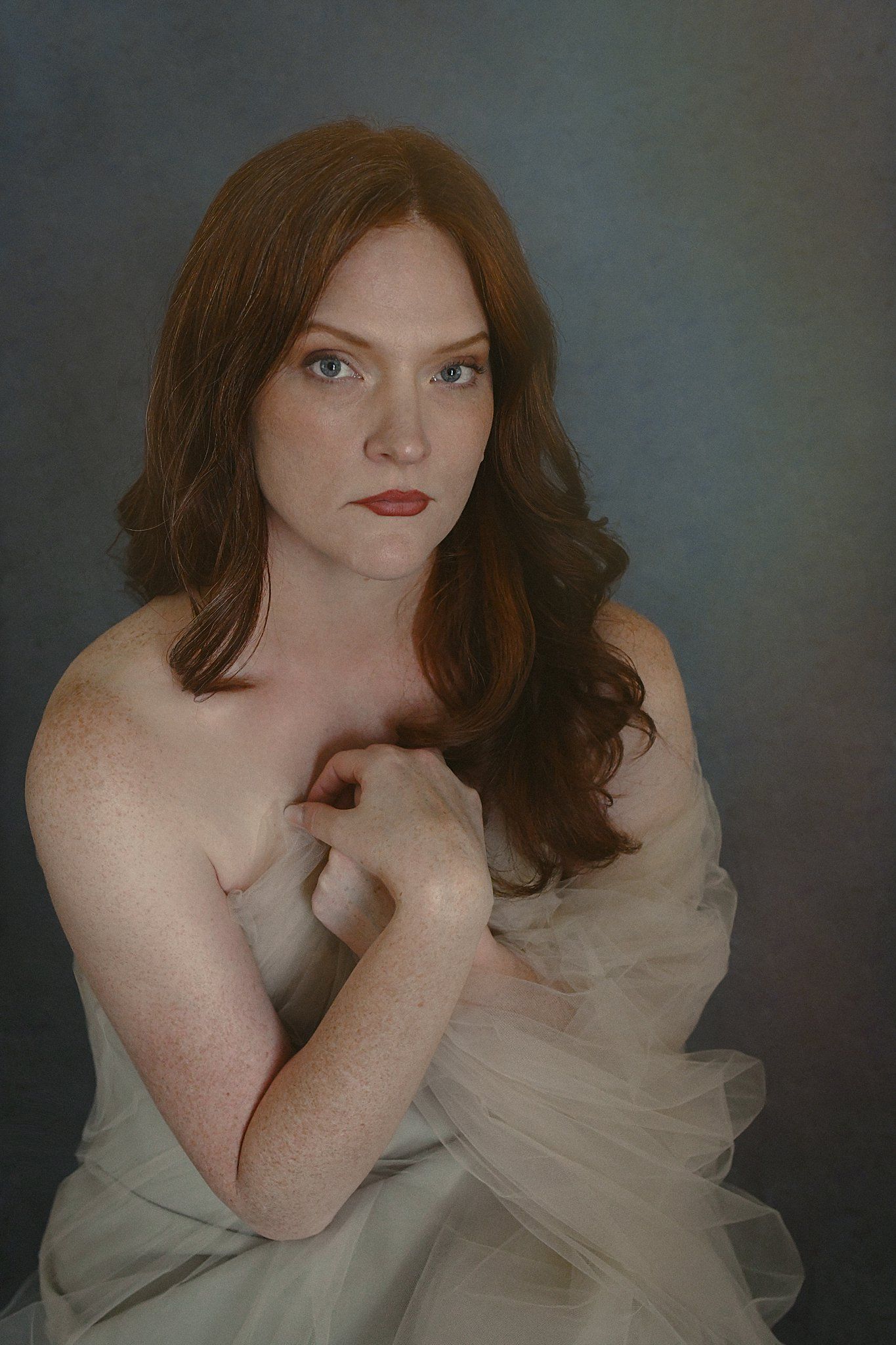 Portrait of someone wearing a white flowing fabric in dramatic lighting with auburn hair.