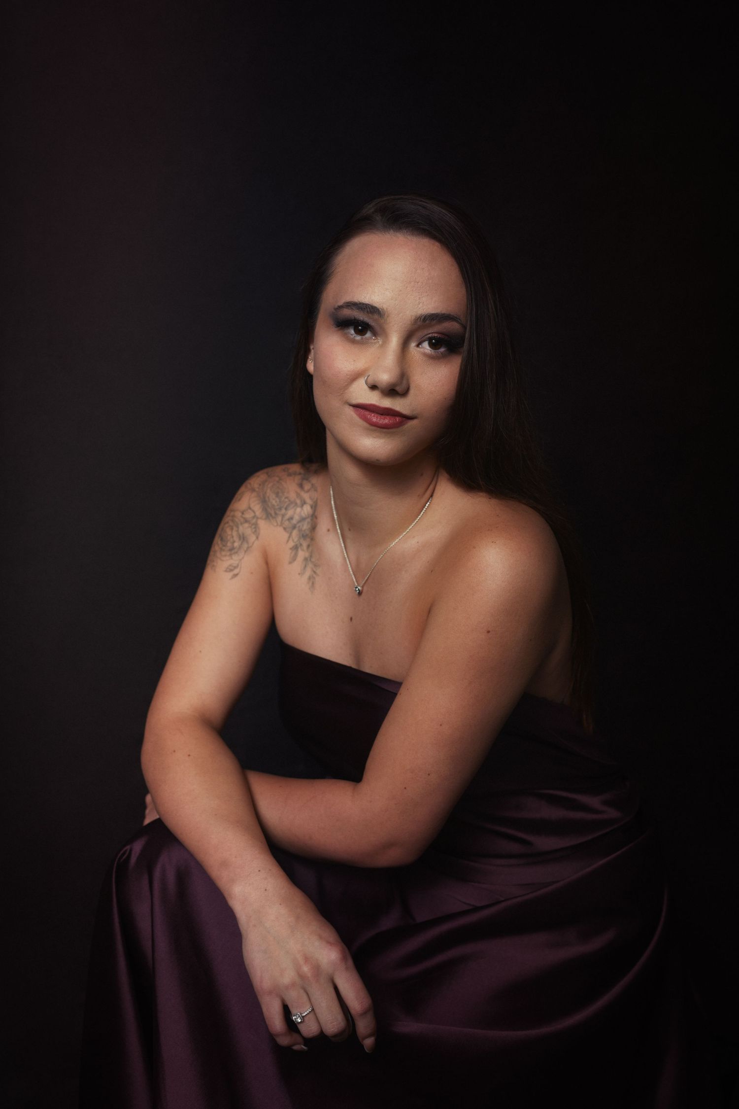An elegant studio portrait featuring a purple satin dress and delicate jewelry against a dark backdrop.