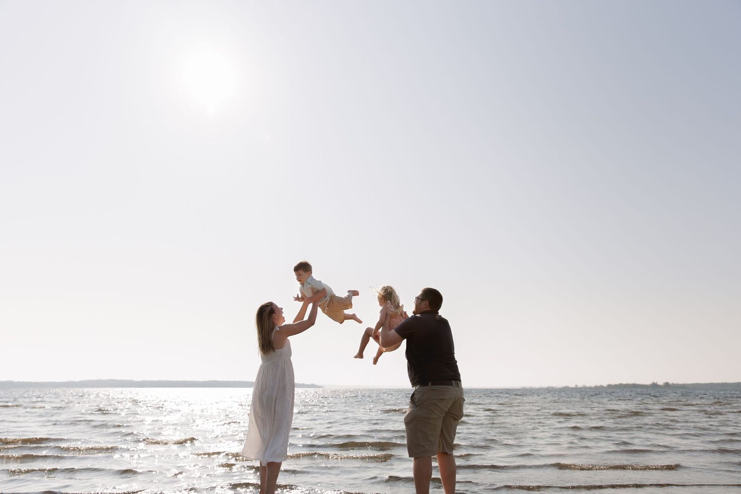 Silhouetted family playing together at sunset on a beach with sun glowing over ocean horizon.