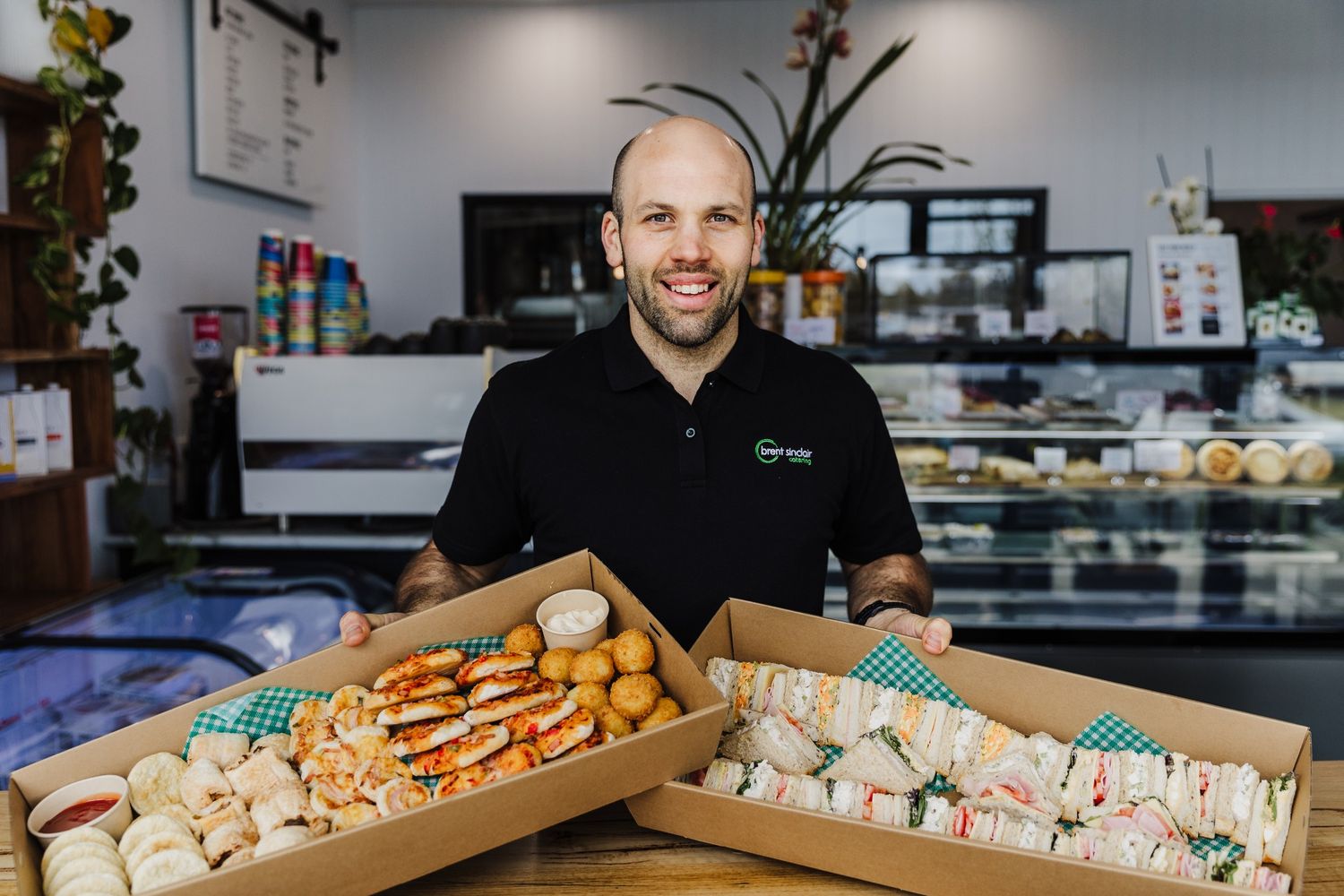 A bakery worker displays fresh baked goods and pastries in wooden boxes on a counter.