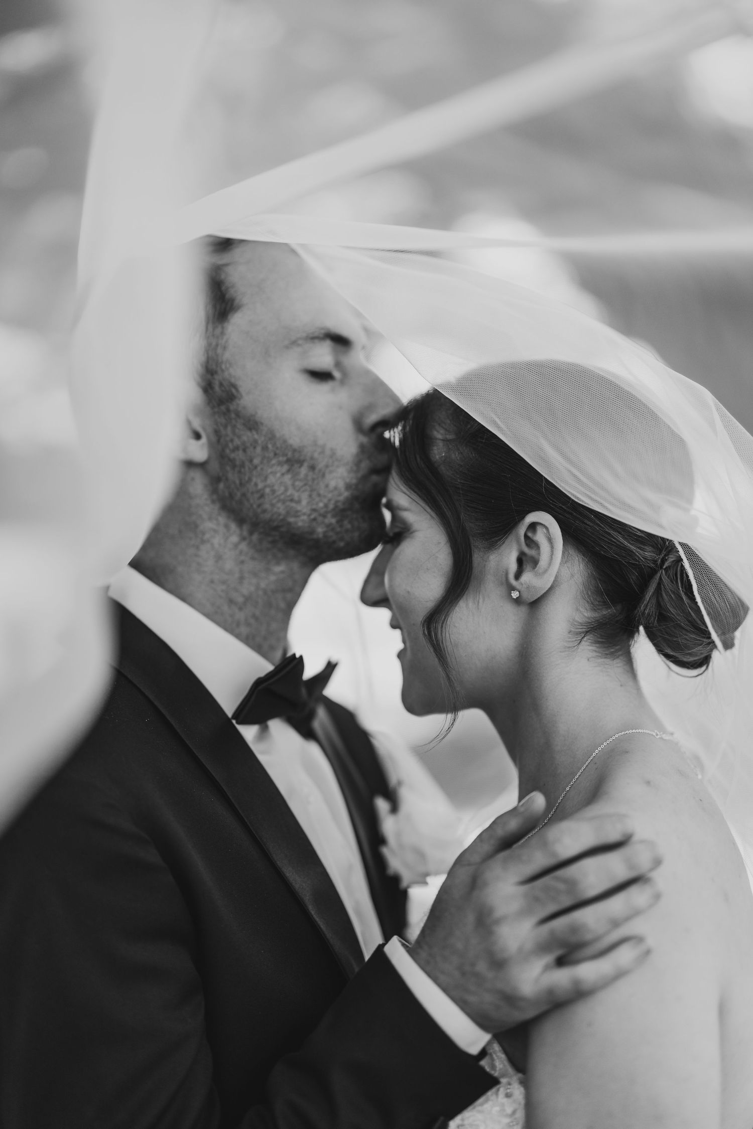 Black and white photo showing a tender moment at a wedding with close-up profile shot of romantic kiss between newlyweds.