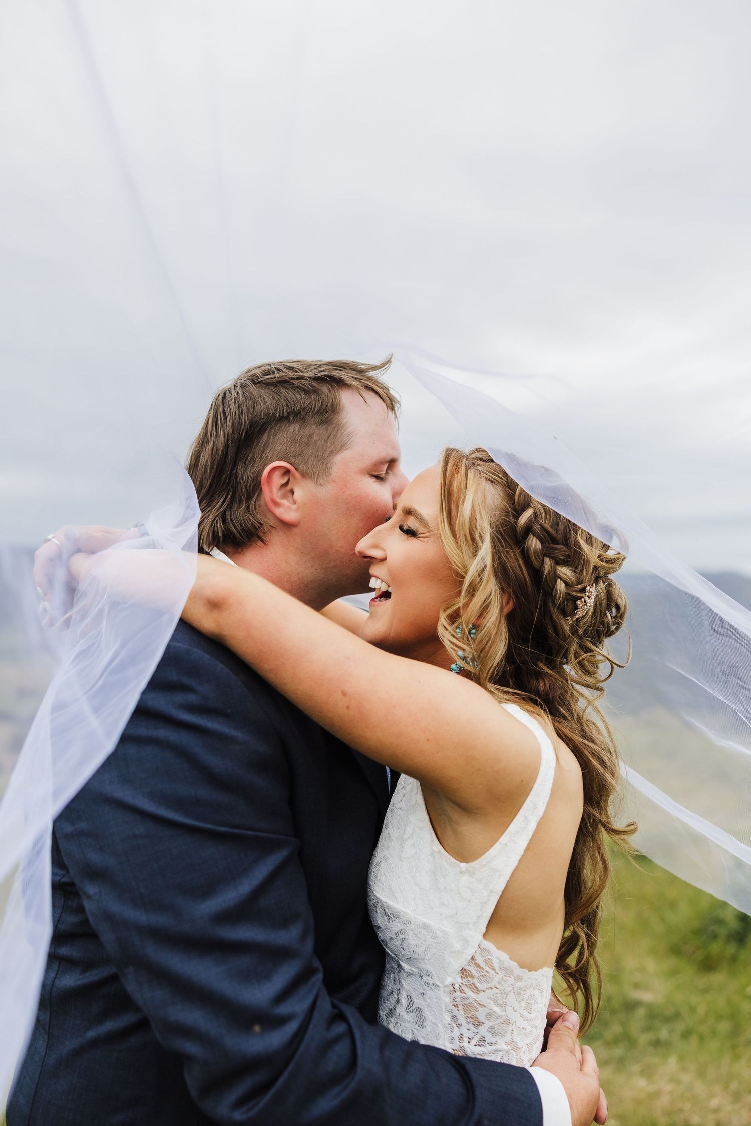 A joyful wedding moment captured outdoors as a couple embraces under a flowing veil on their special day.