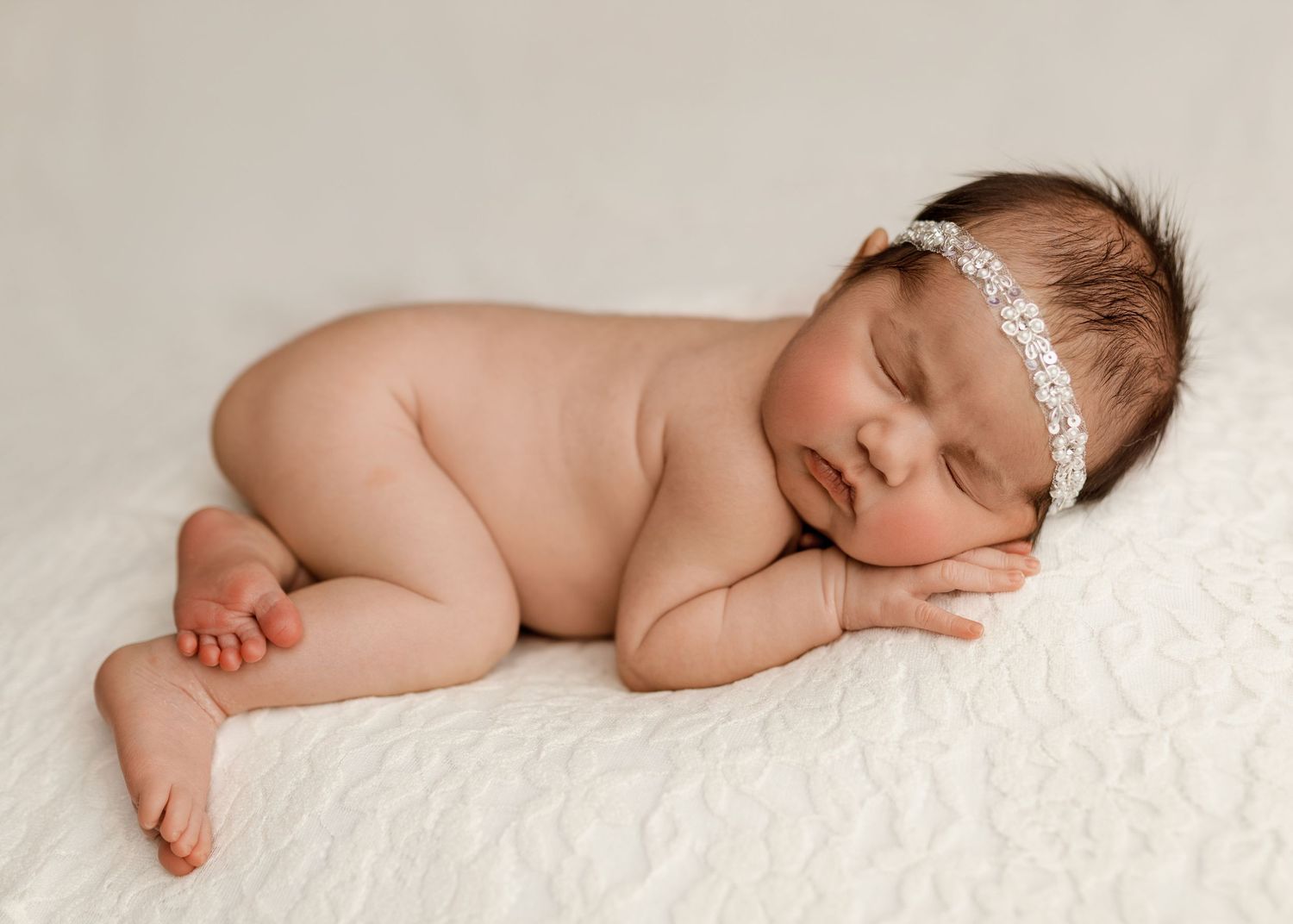Peaceful newborn baby girl sleeping on white fluffy blanket wearing a delicate floral headband.