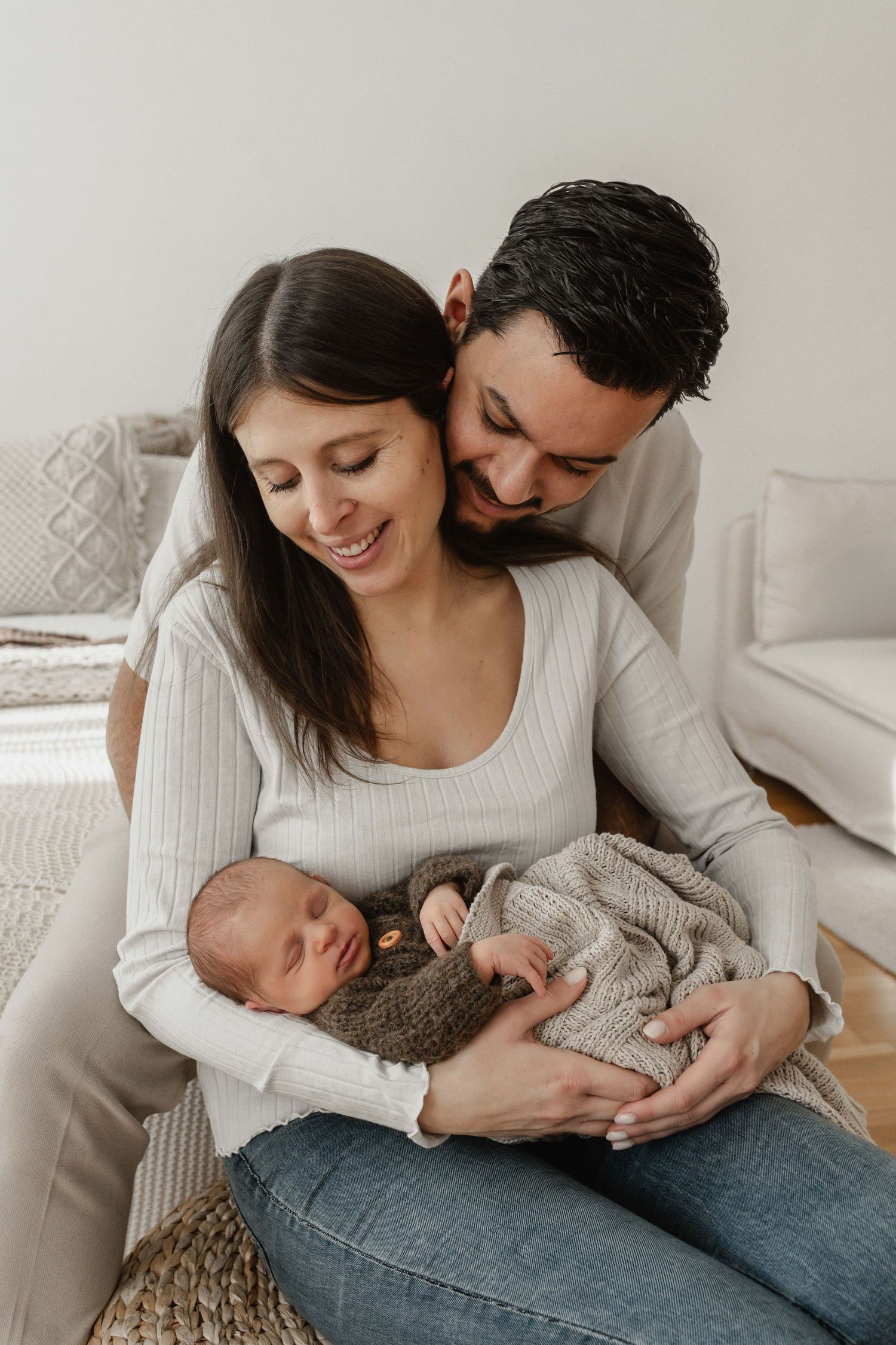 Schlafendes Neugeborenes im Arm der Mutter, begleitet von den Eltern bei einem ruhigen Newbornshooting im Studio in Stockerau