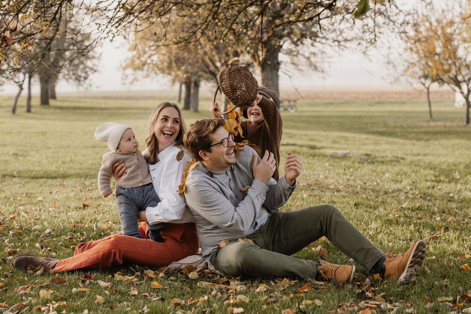 Familie sitzt im Herbst auf Wiese zwischen Apfelbäumen, Eltern lachen mit ihrem Kind bei  lebendigen Familienfotografie outdoor Stockerau
