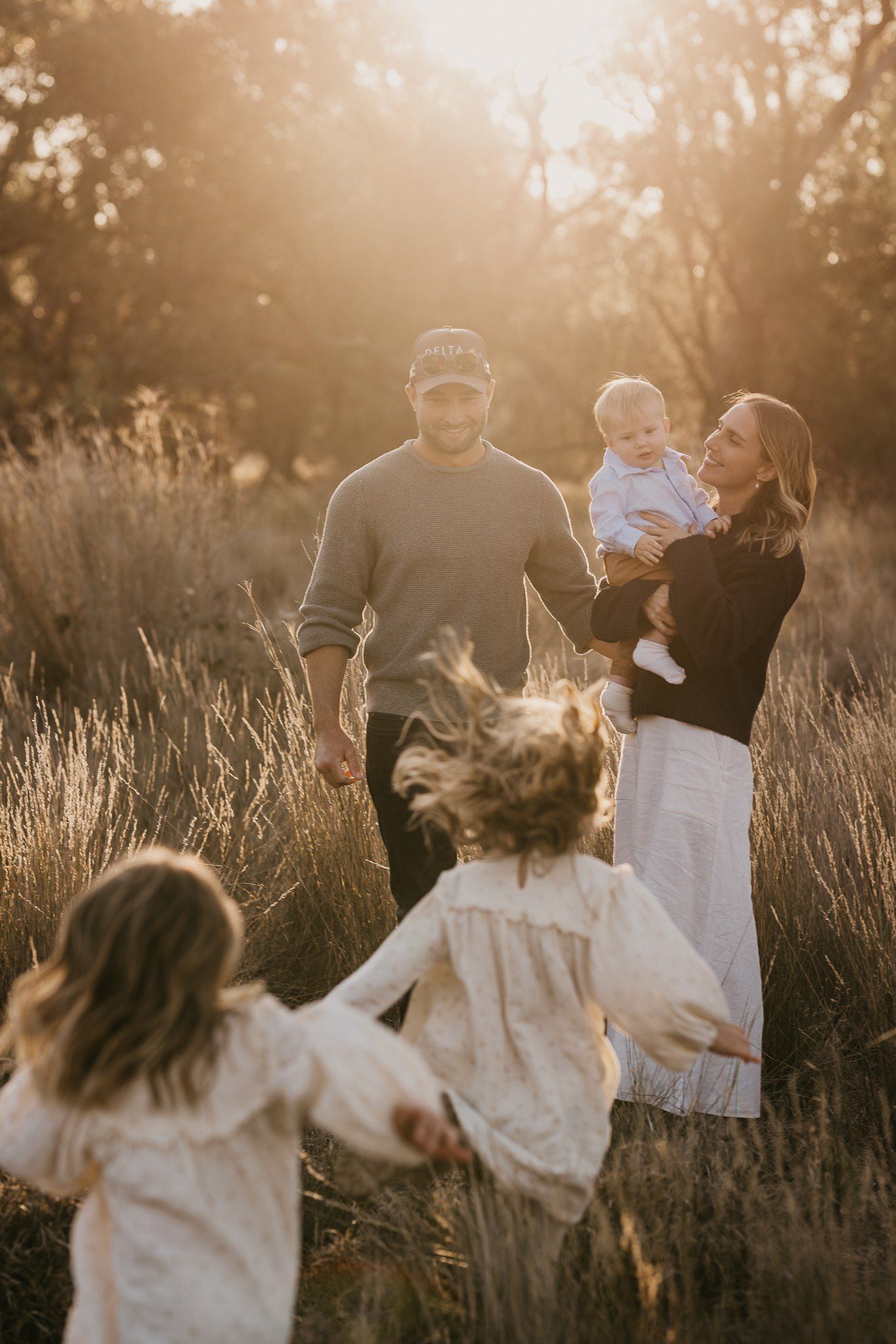 Family walking through golden paddock grass at sunset during a rural family photography session near Gulargambone NSW