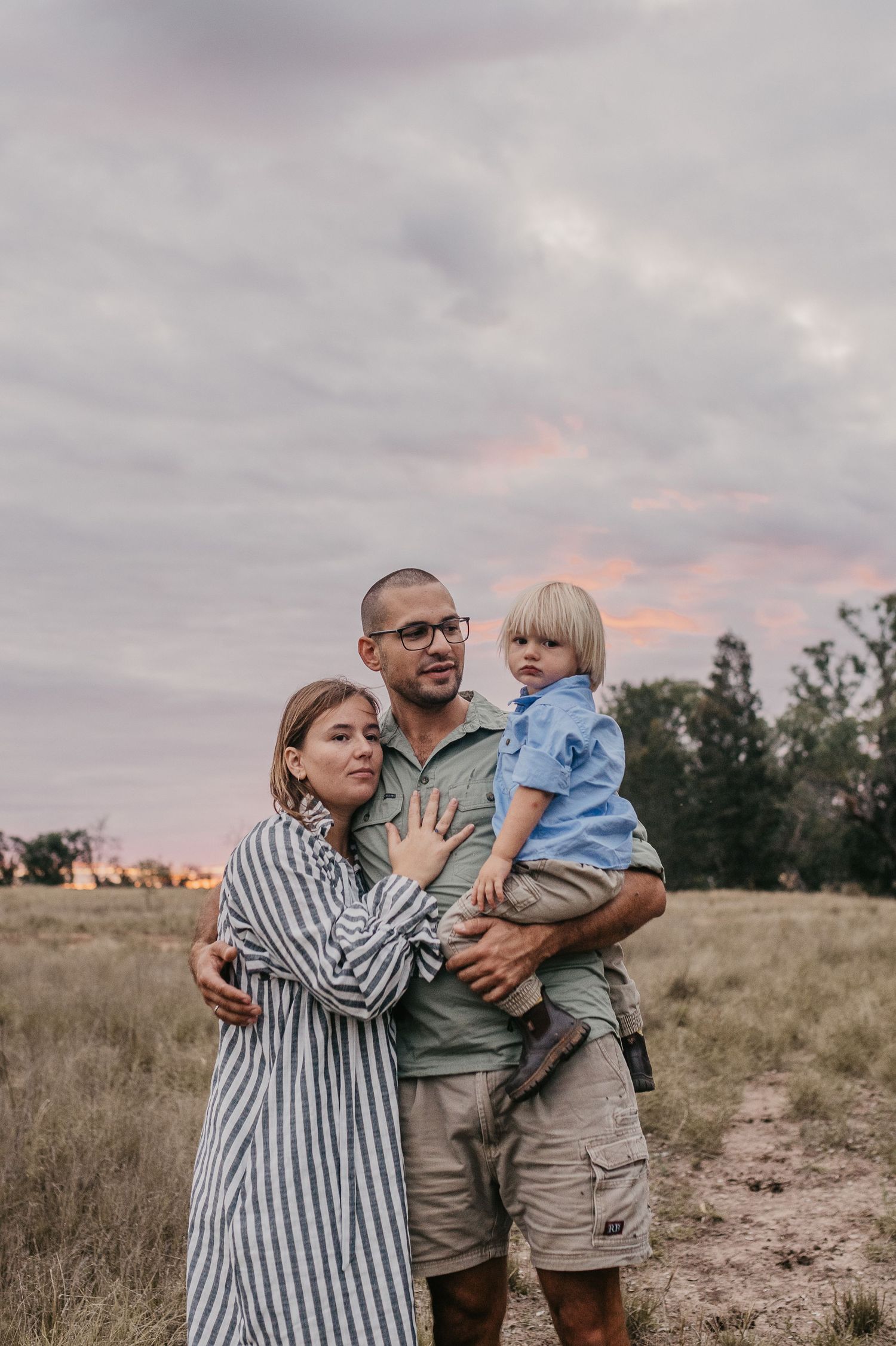 a family standing in a rural paddock at sunset.