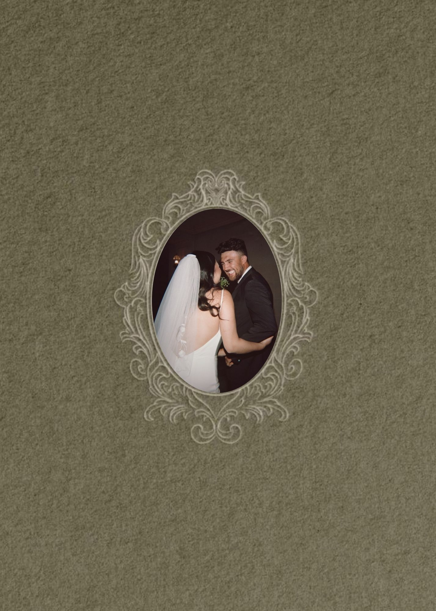 A vintage-style oval ornate frame on a olive green background displays a portrait of a bride and groom embracing.