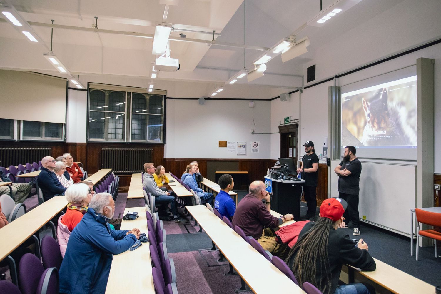 Students watch a presentation on multiple screens in a modern classroom setting during a lecture.