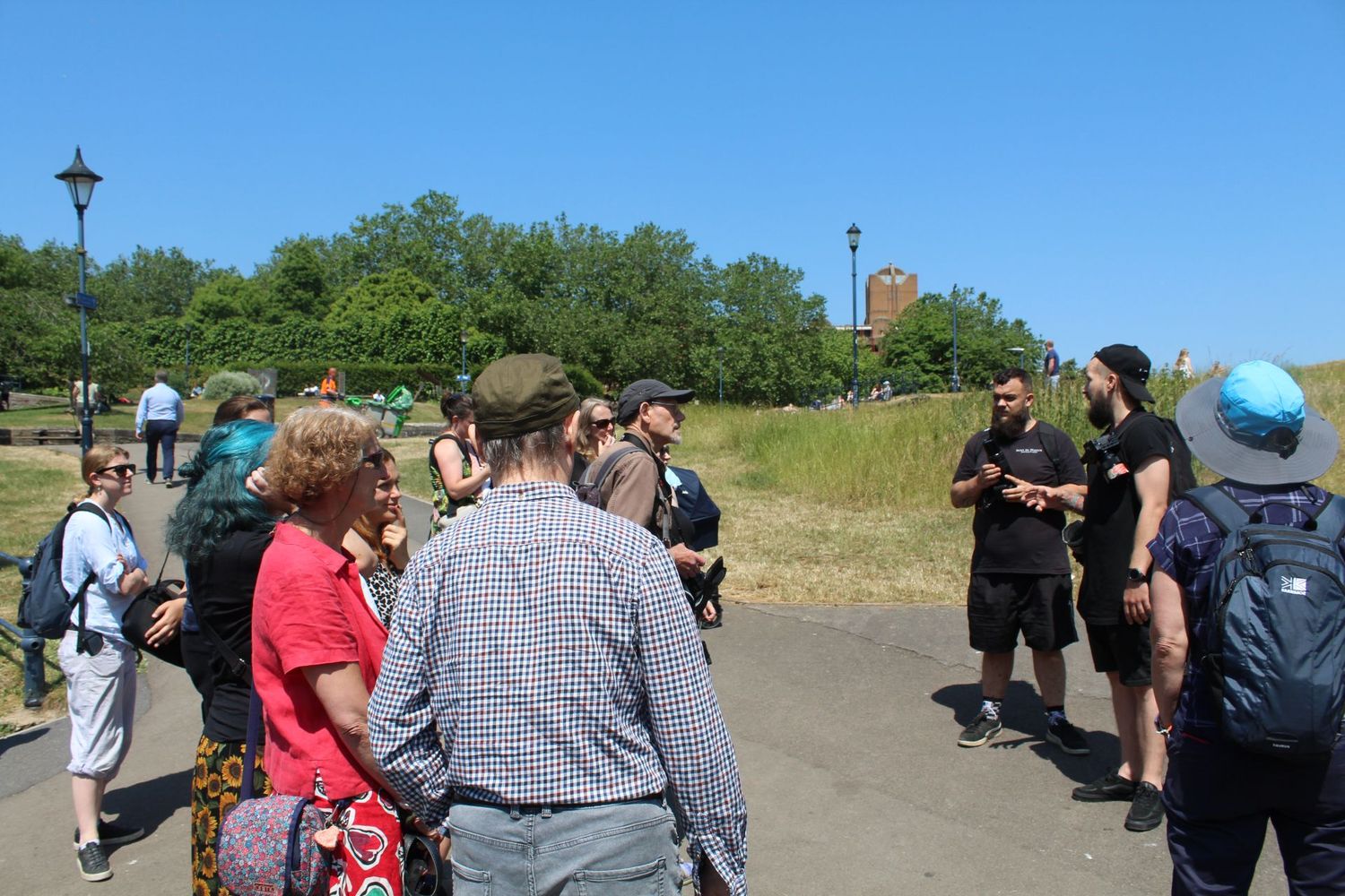 A group of people gather outdoors for a guided nature walk along a hillside path on a sunny day.