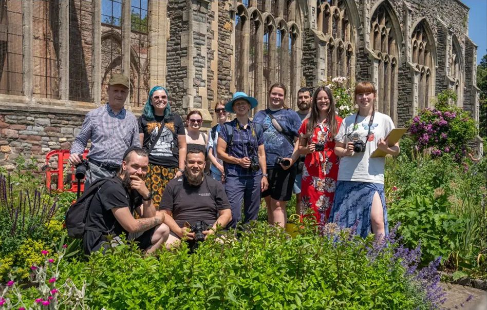 A group gathers in a garden area near a Gothic-style church or cathedral with ornate stone architecture.