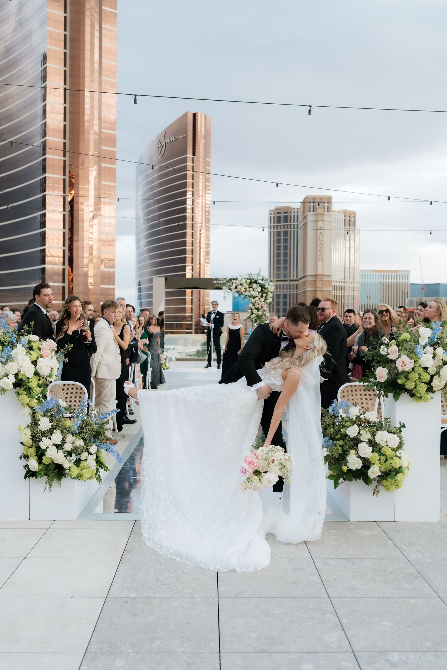Bride and groom share a romantic dip kiss at an elegant rooftop wedding ceremony with Las Vegas skyline backdrop.