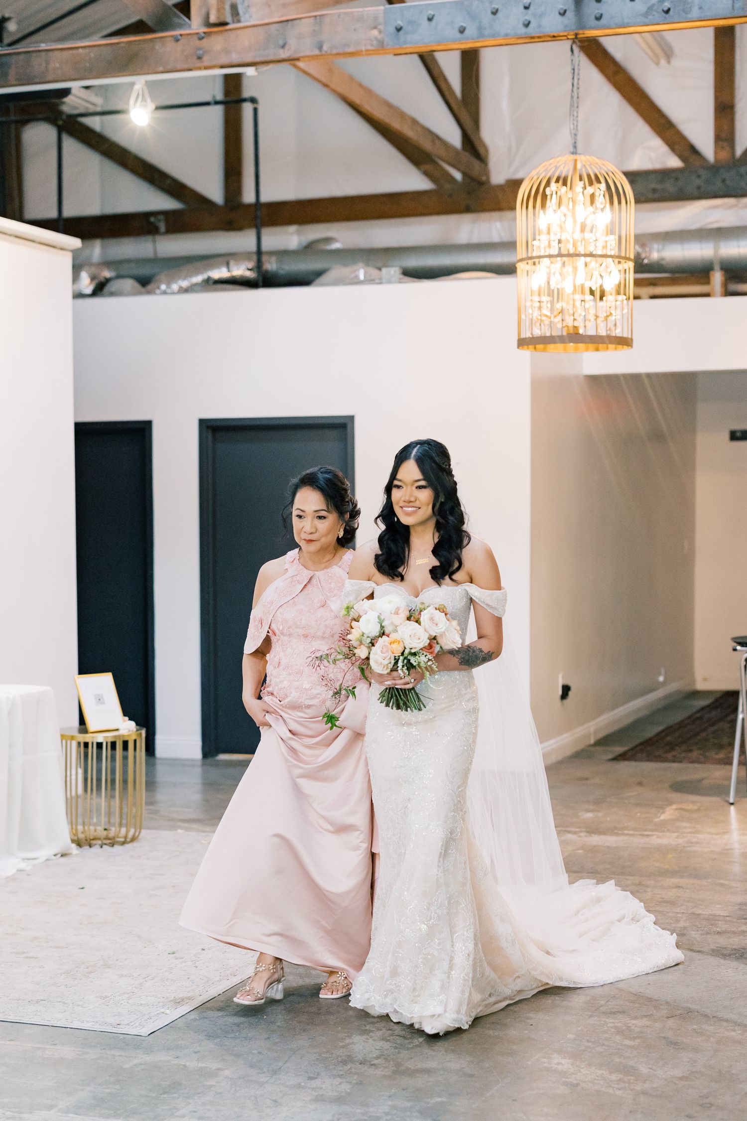 Wedding party walking through modern venue with elegant chandeliers and white walls.