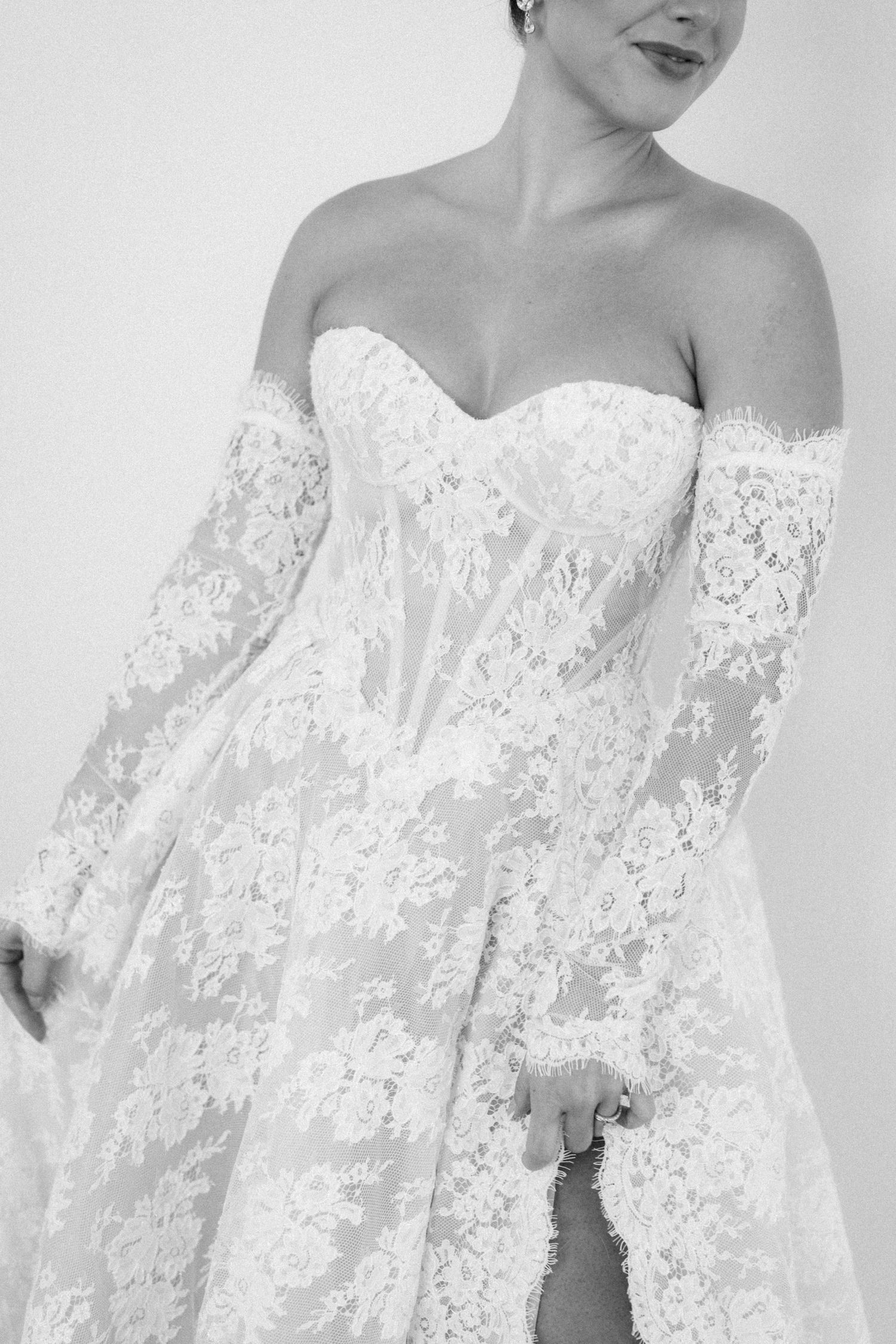 Black and white photo of a bride wearing an elegant off-shoulder lace wedding gown with long sleeves.