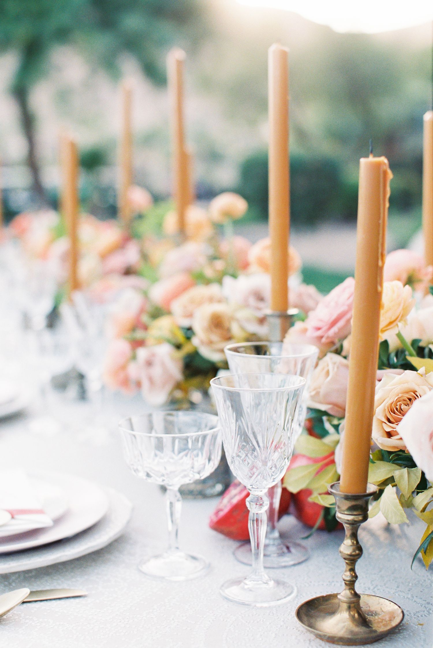 Elegant wedding tablescape with crystal glasses, gold taper candles, and blush floral centerpieces on a silver linen.