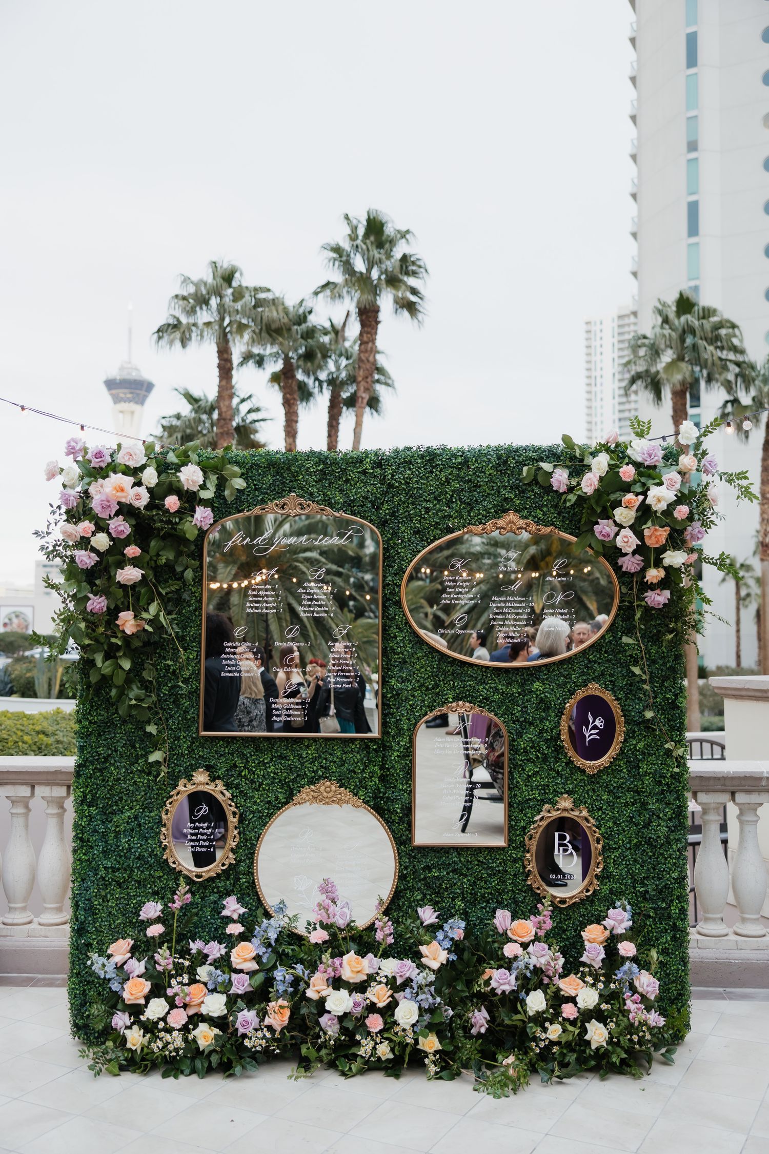 Elegant hedge wall wedding seating chart with gold mirrors, pastel florals, and Las Vegas skyline backdrop.