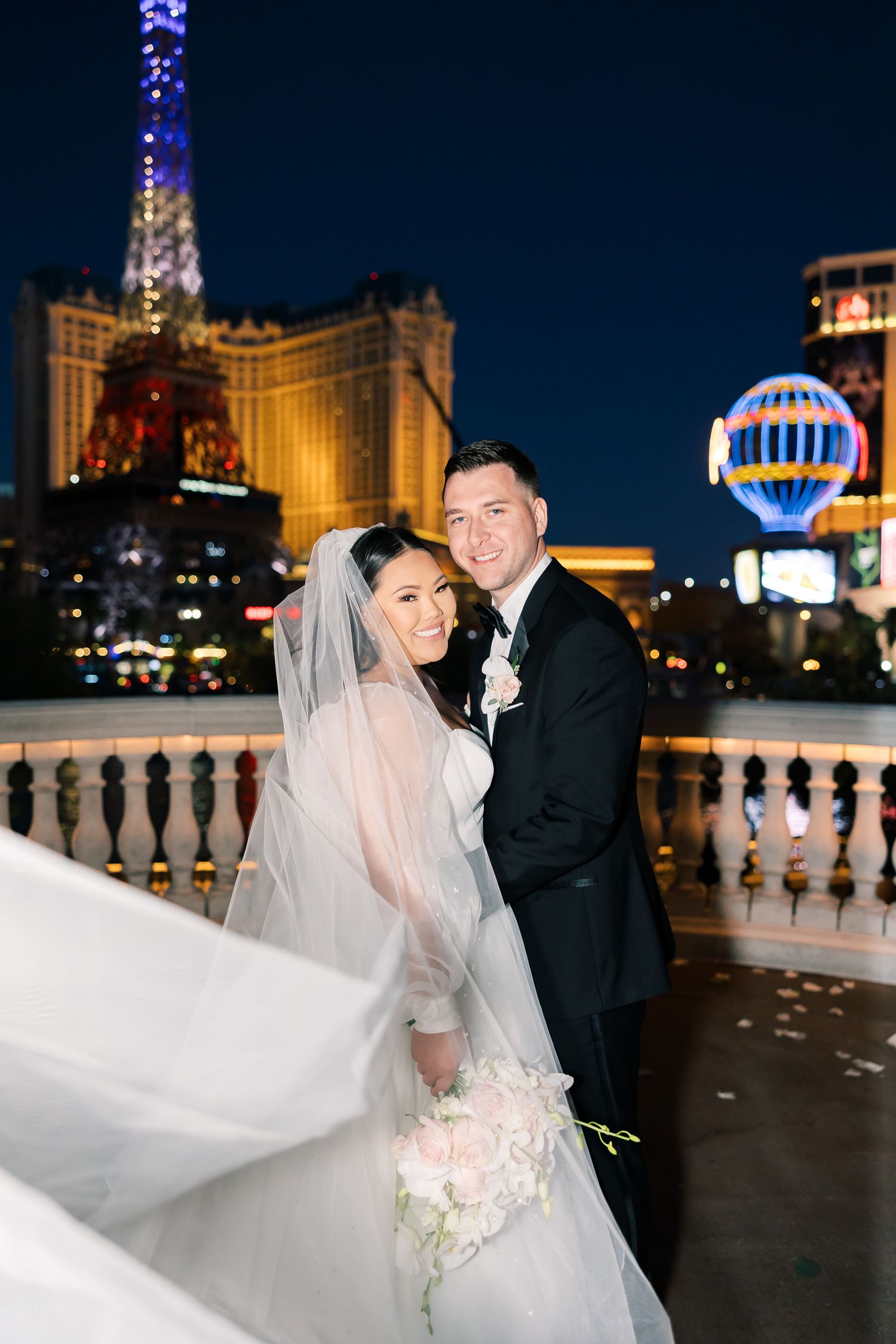 Bride and groom pose together at night on the Las Vegas Strip, with the Eiffel Tower replica glowing behind them.