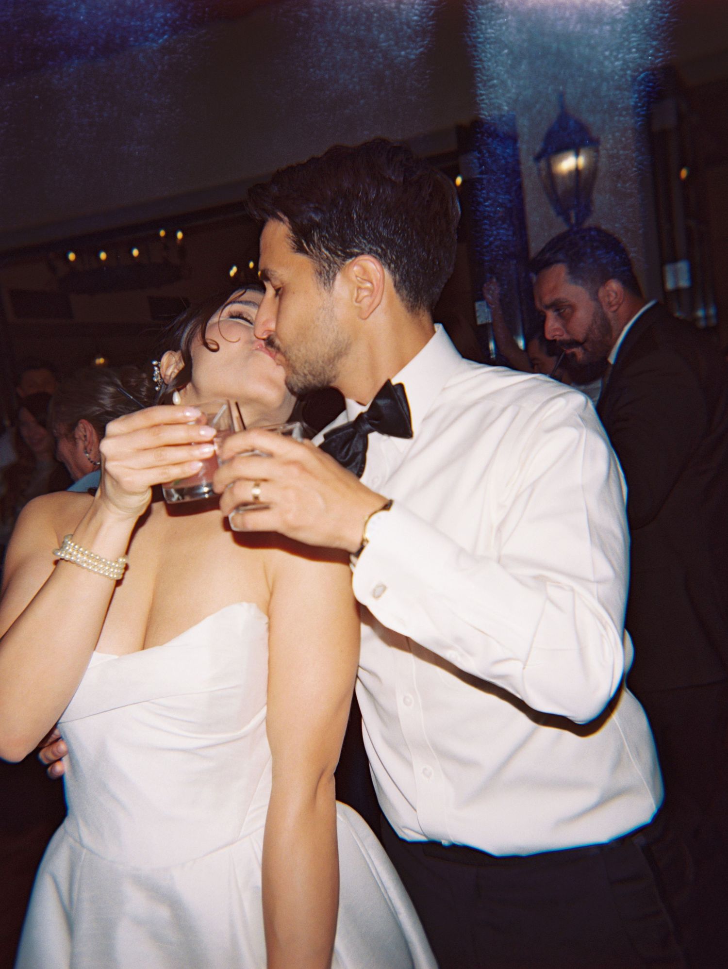 Bride and groom sharing a kiss while holding drinks at their wedding reception dance floor.