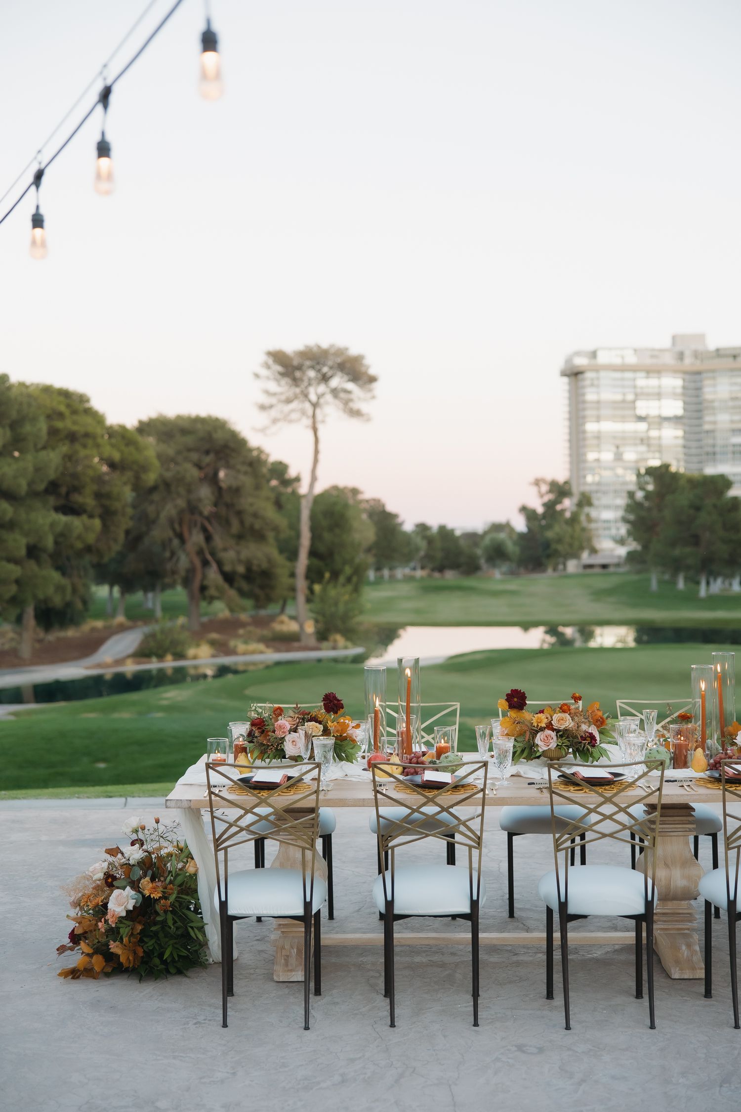 Elegant outdoor wedding reception table set with candles, floral arrangements, and string lights overlooking a golf course.