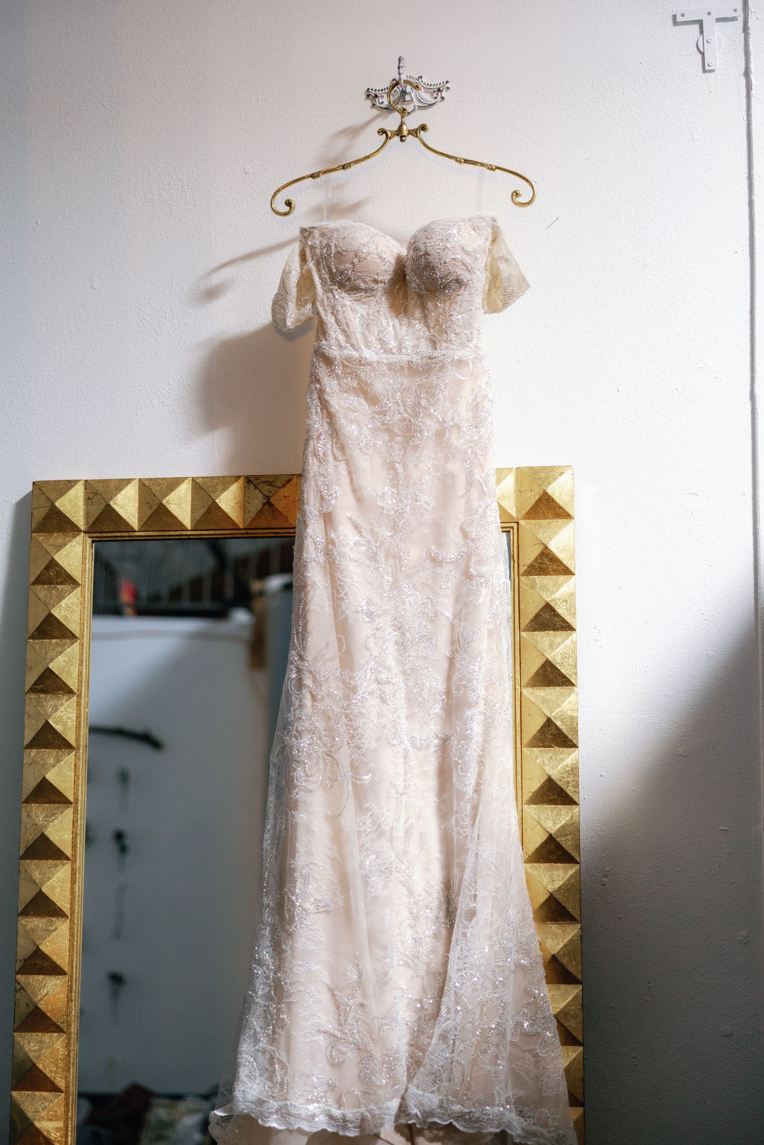 Elegant white lace wedding dress hanging on display against a wall with gold geometric decorative elements.