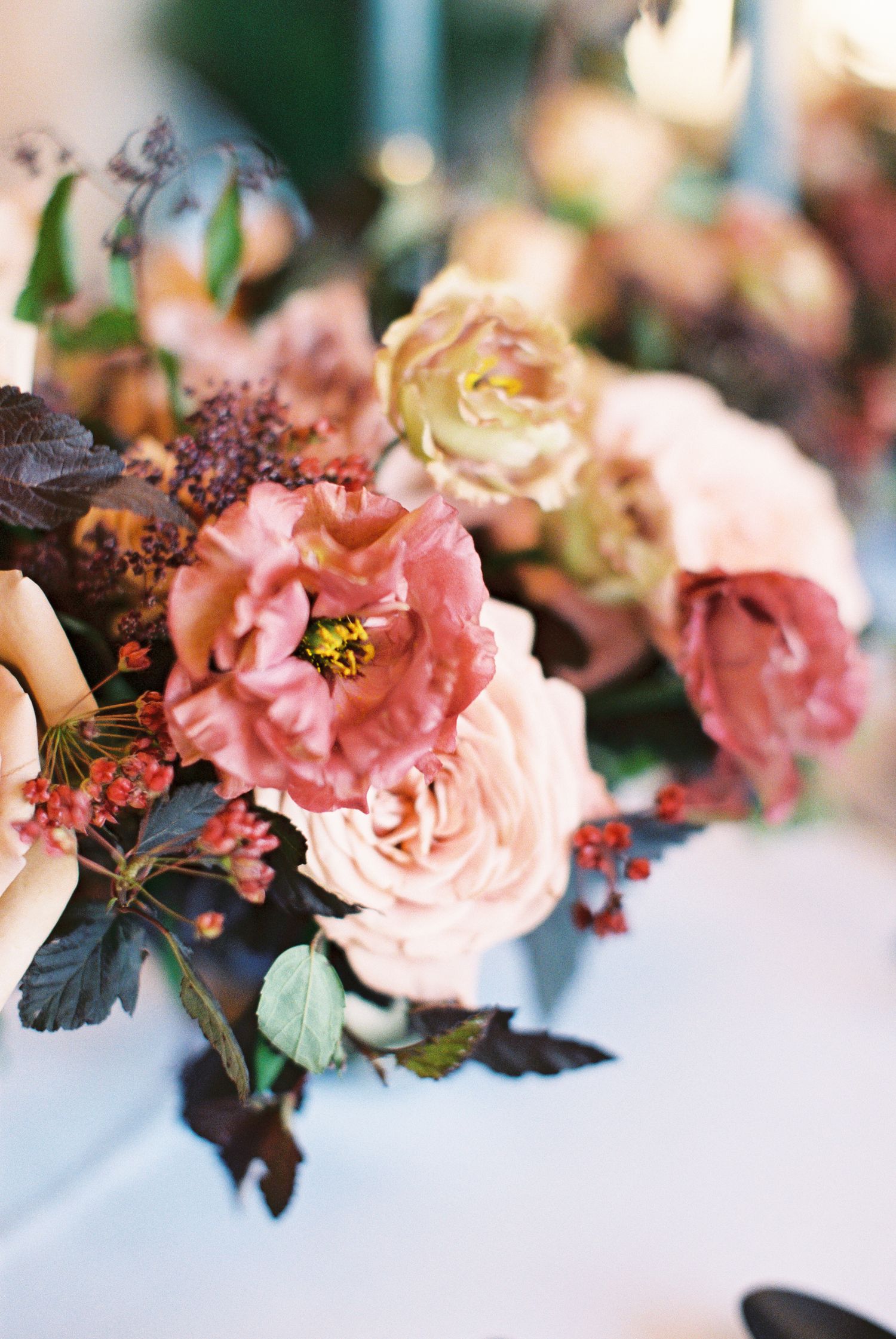 Elegant floral centerpiece with dusty pink and blush roses, dark foliage, and red berries for a romantic wedding table.