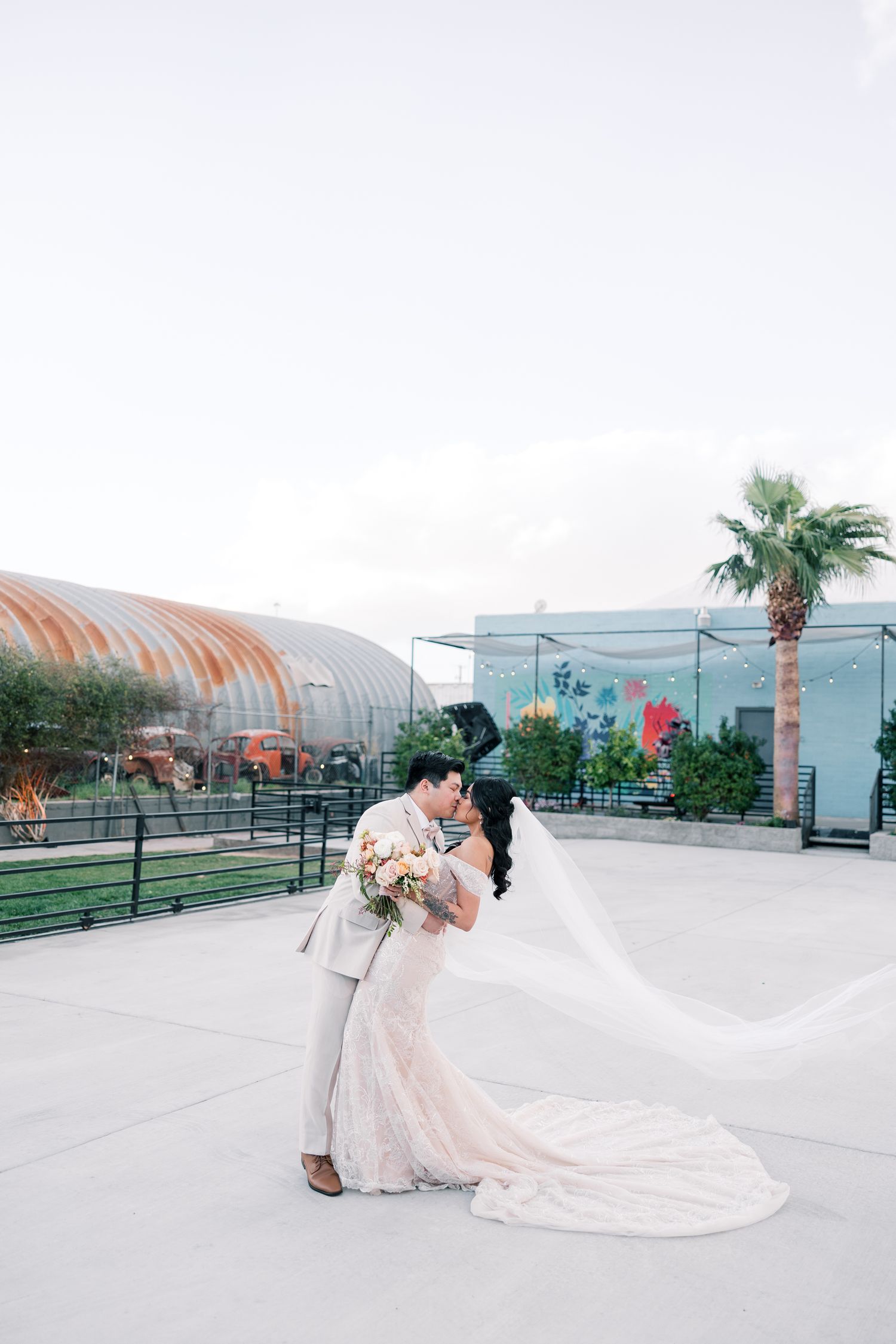 Wedding couple poses on modern rooftop venue with curved architectural structures and palm trees.