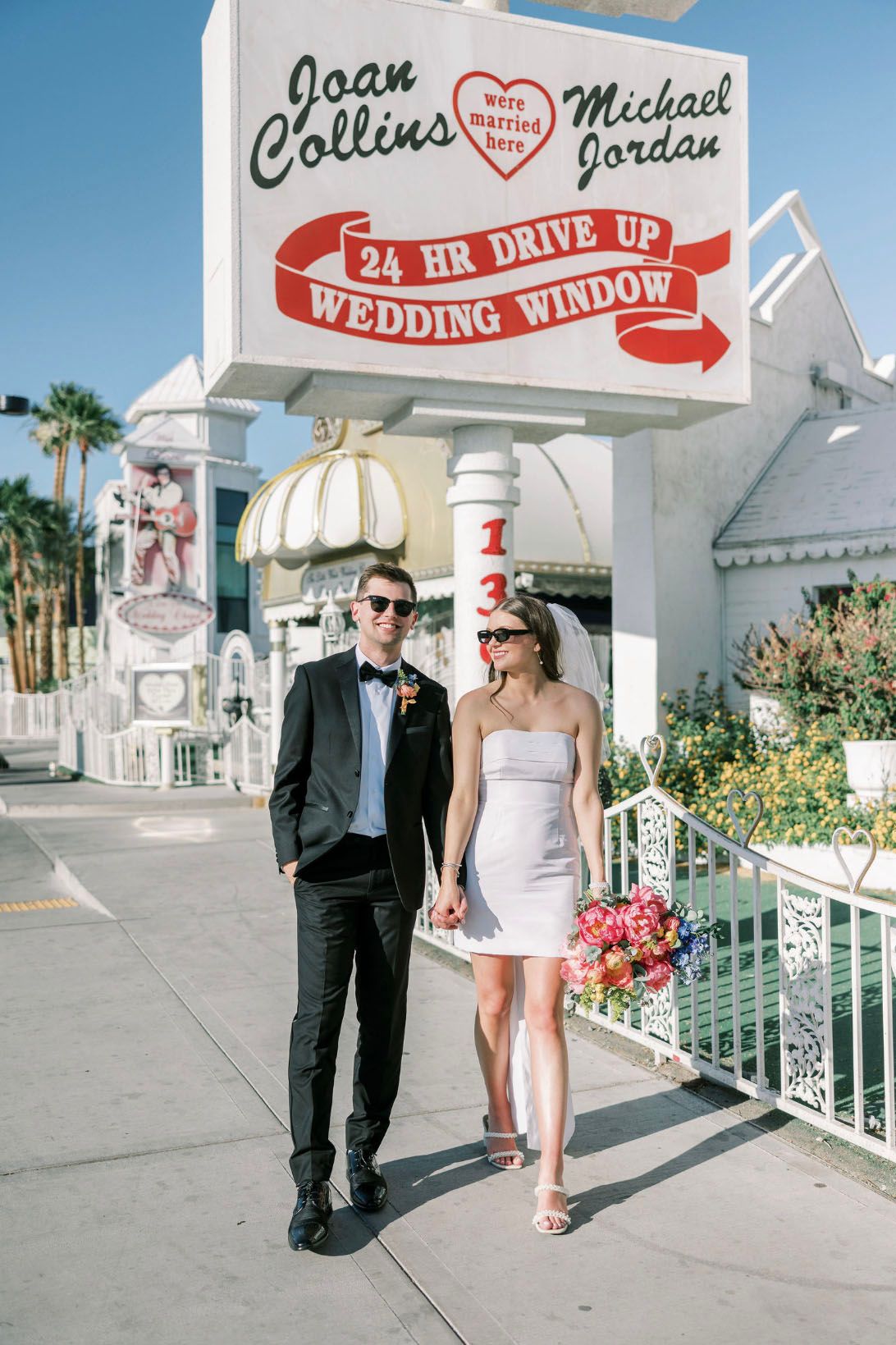Couple poses at Las Vegas 24-hour drive-up wedding window chapel beneath Joan Collins and Michael Jordan married here sign.