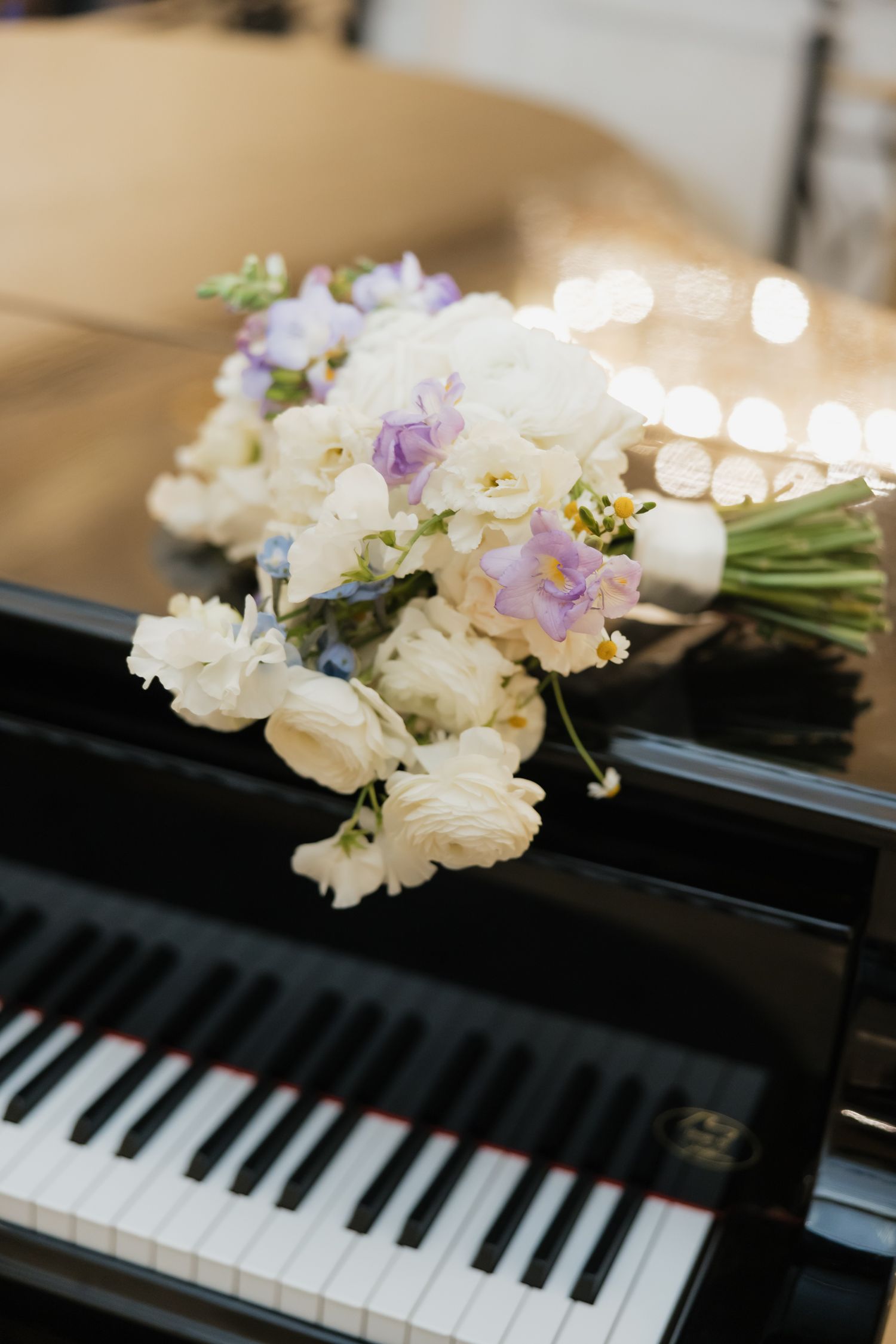 An elegant bridal bouquet of white and lavender flowers rests on a black grand piano keys.