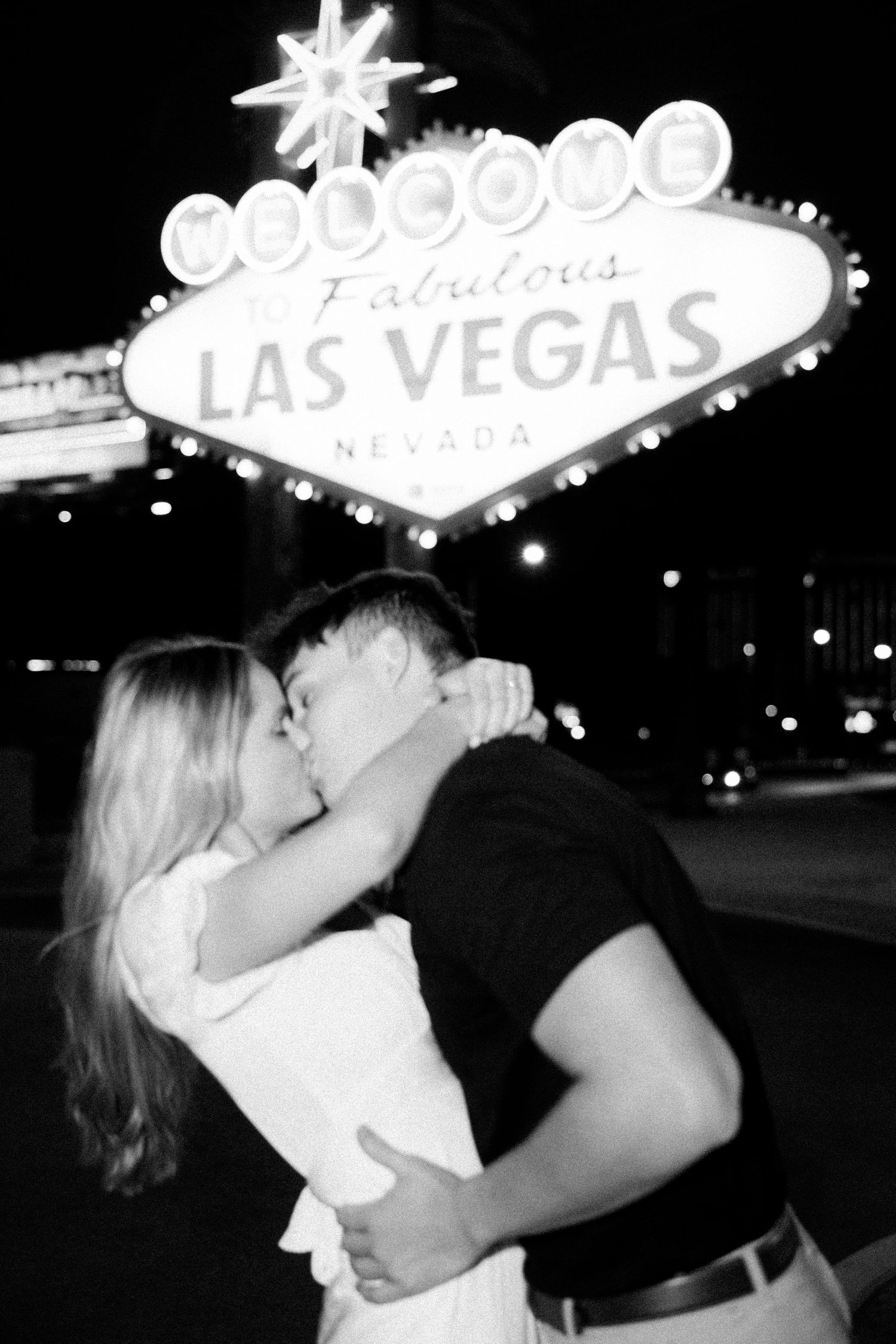 Couple kissing in front of the iconic Welcome to Fabulous Las Vegas Nevada sign at night in black and white.