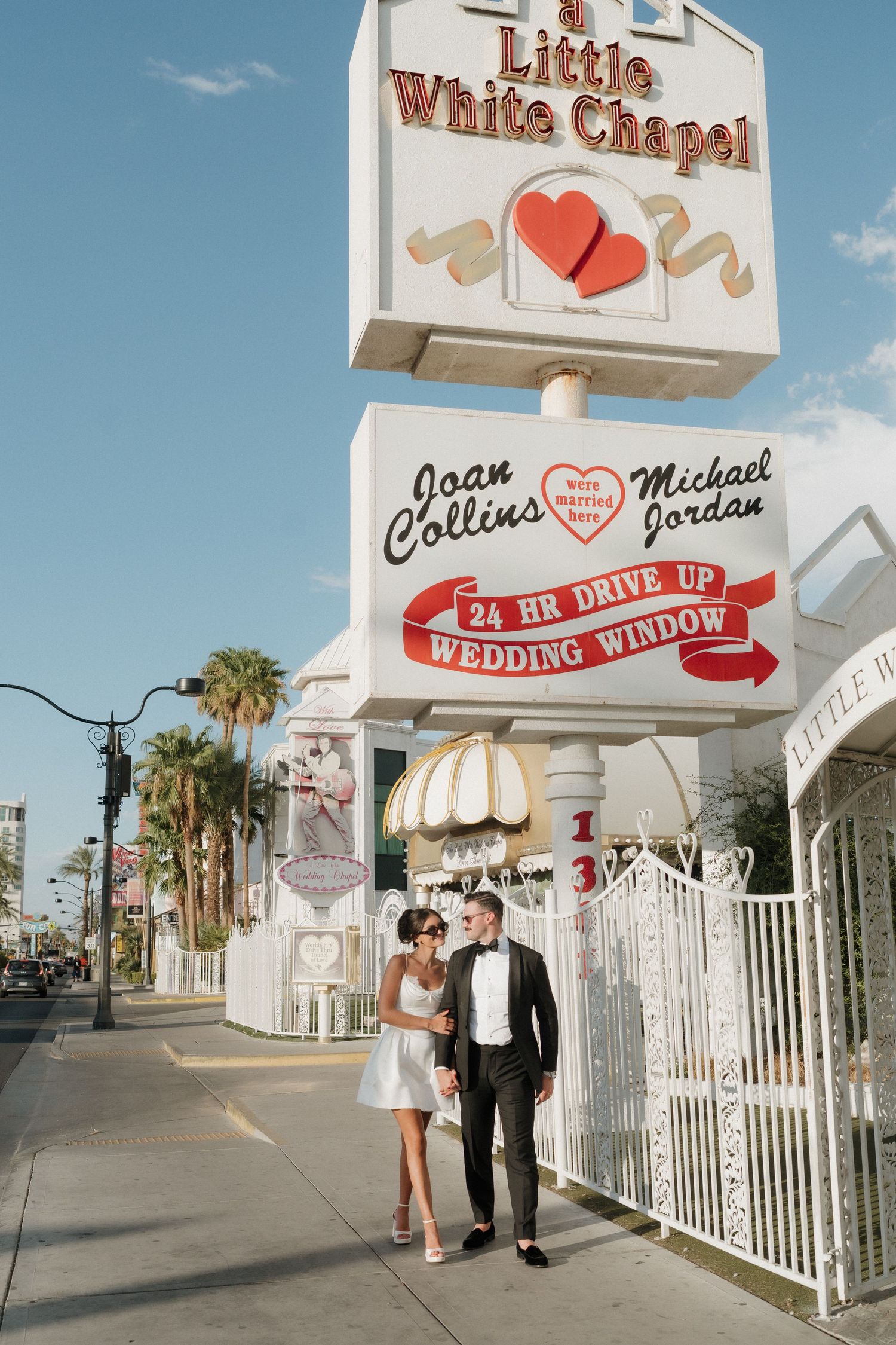 Couple poses in front of A Little White Chapel 24-hour drive-up wedding window in Las Vegas, NV.