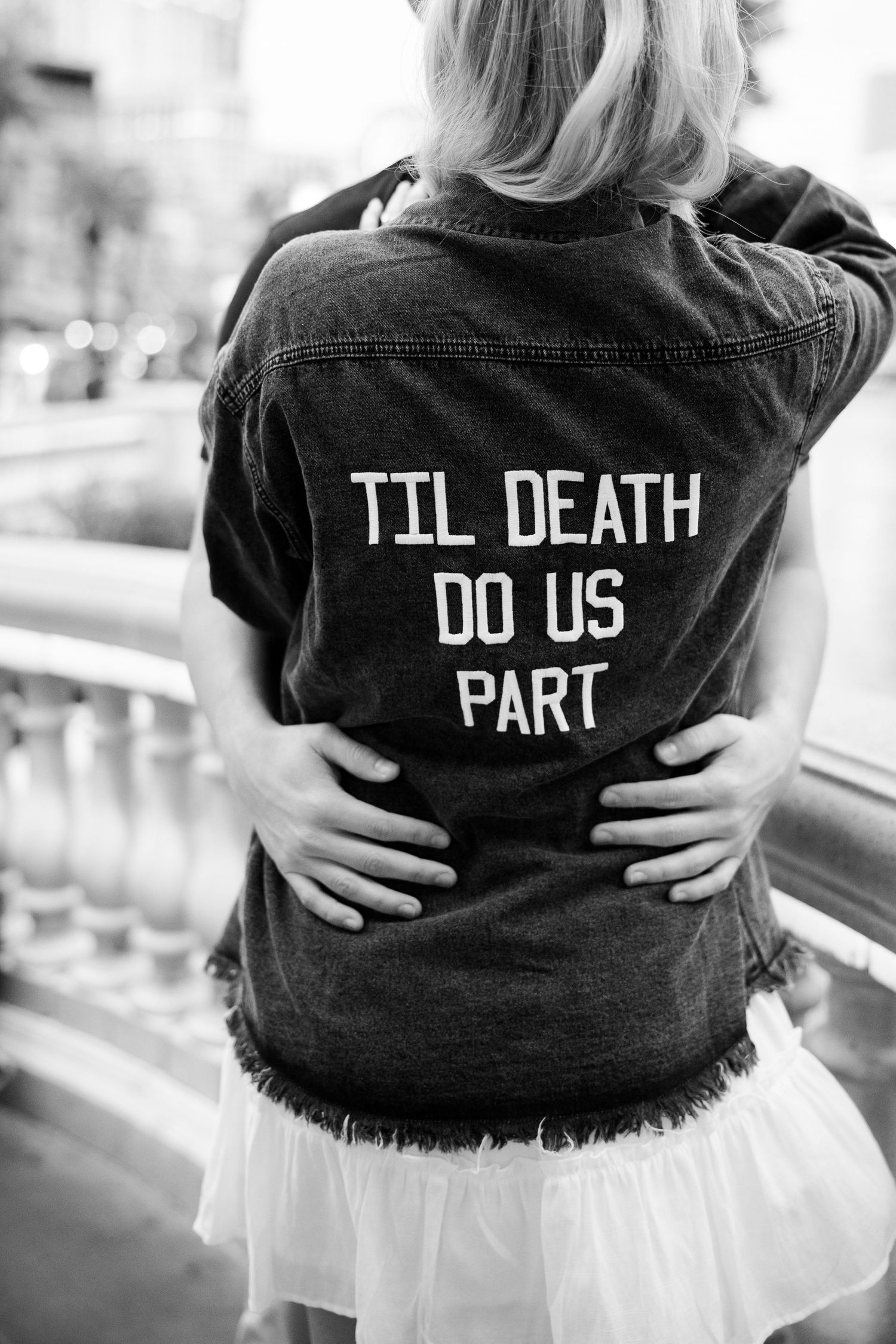 Black and white photo of woman in denim jacket with 'Til Death Do Us Part' text, embraced from behind.