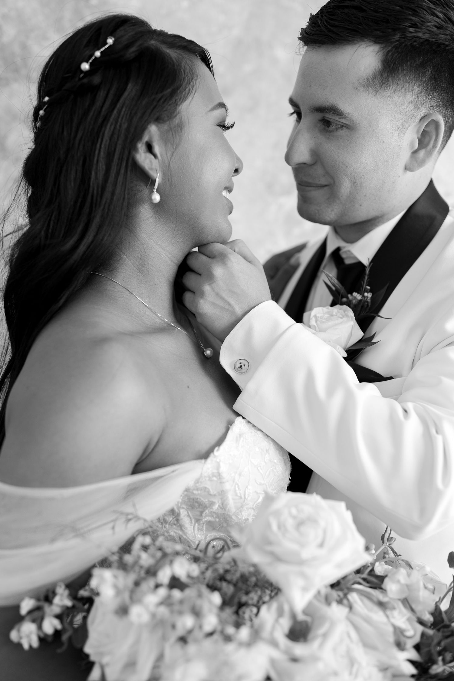 Black and white wedding photo of groom tenderly touching bride's chin while she holds a bouquet of white roses.