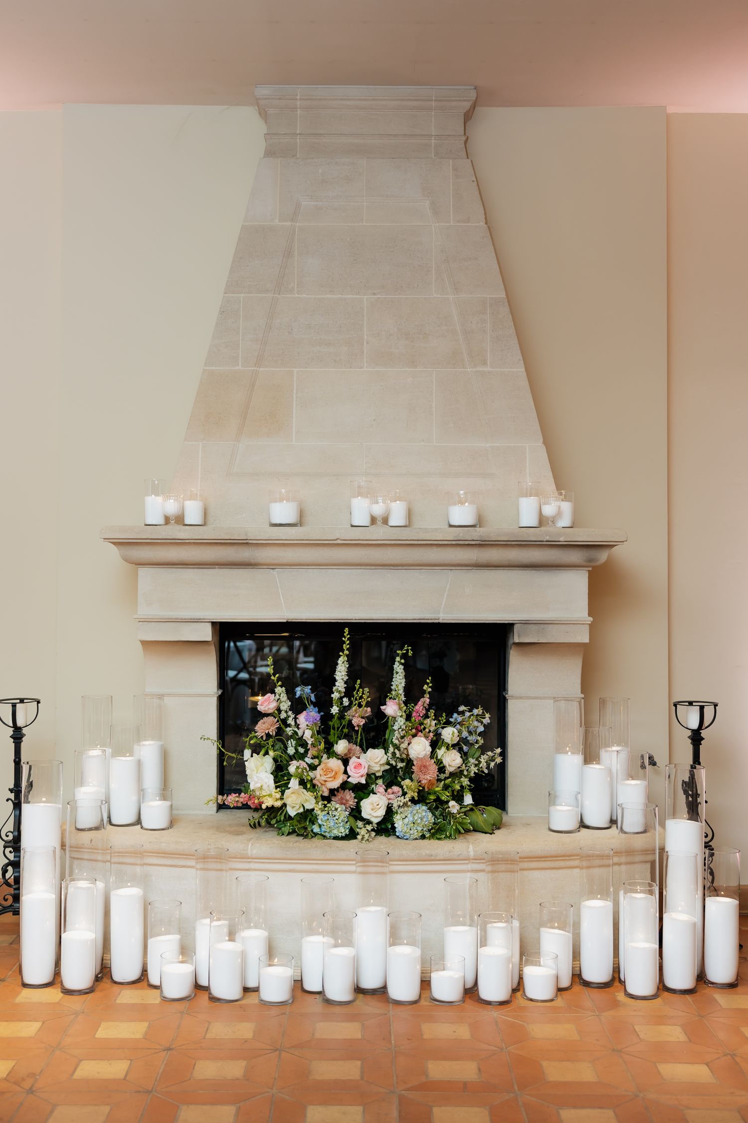 Elegant fireplace decorated with white pillar candles and a lush floral arrangement of pink and green blooms for a wedding reception.