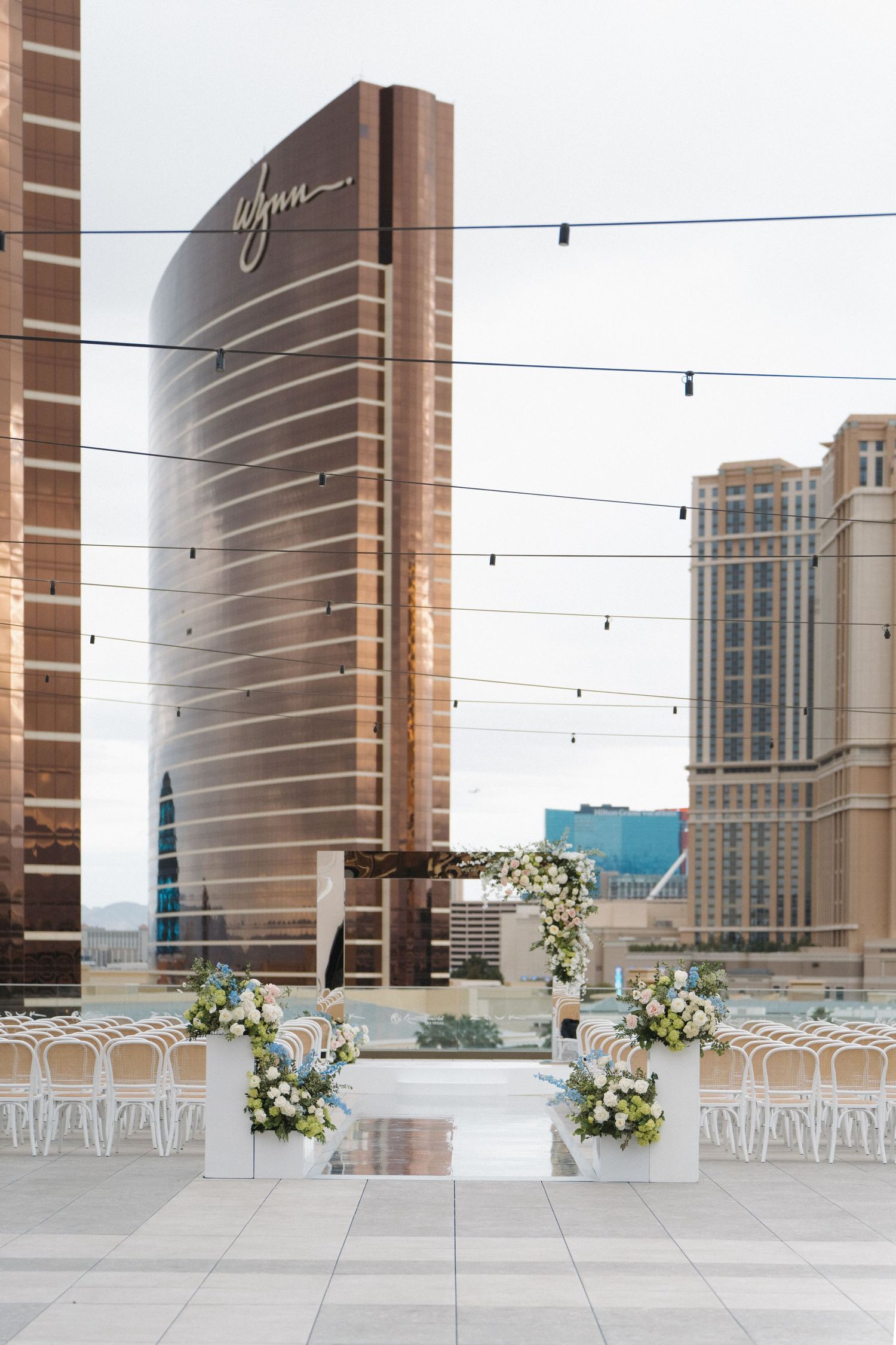 Elegant rooftop wedding ceremony setup with floral arch and city skyline views, featuring the Wynn Las Vegas hotel.