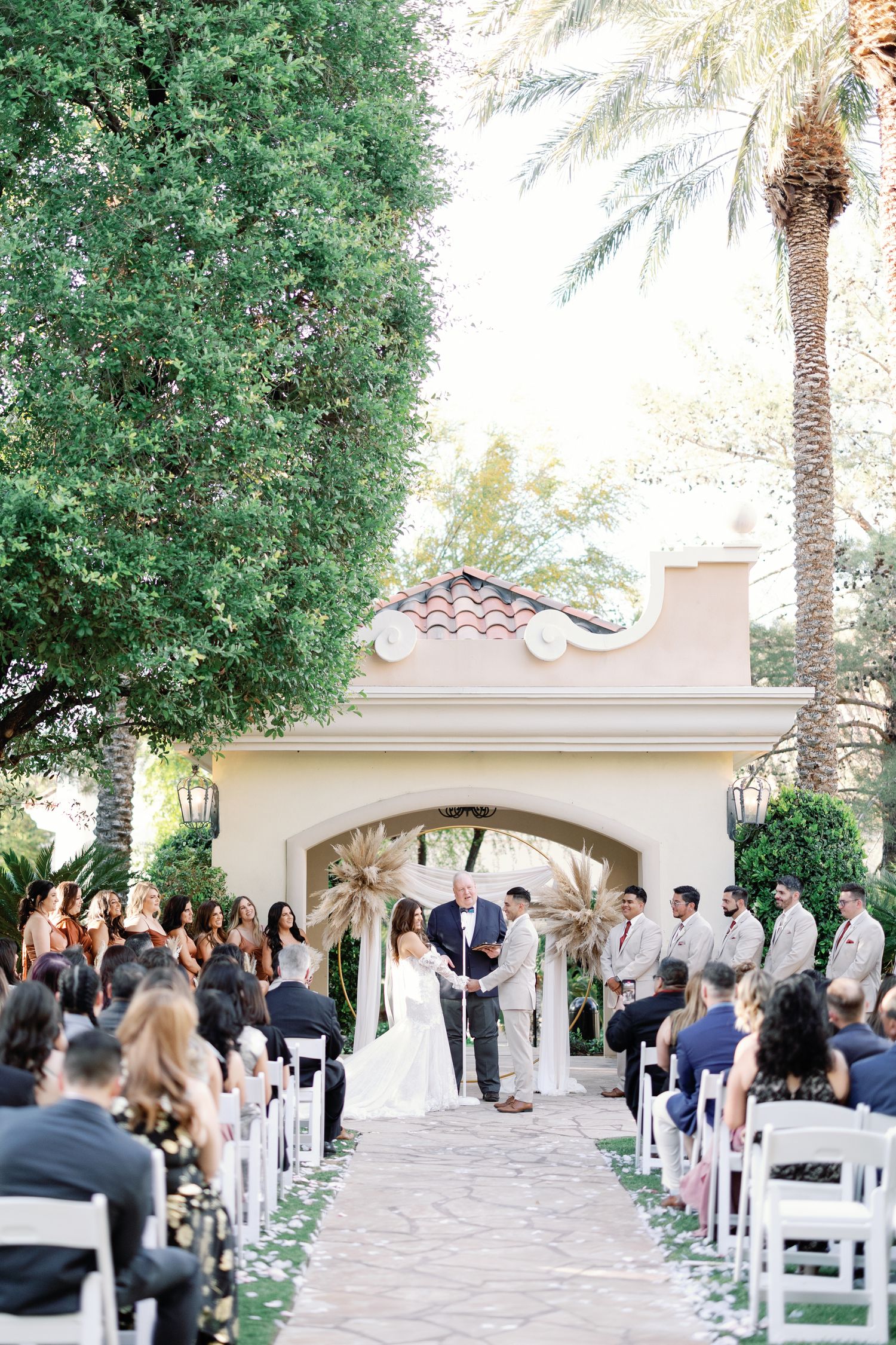 Outdoor wedding ceremony with guests seated along an aisle leading to an elegant arch altar.