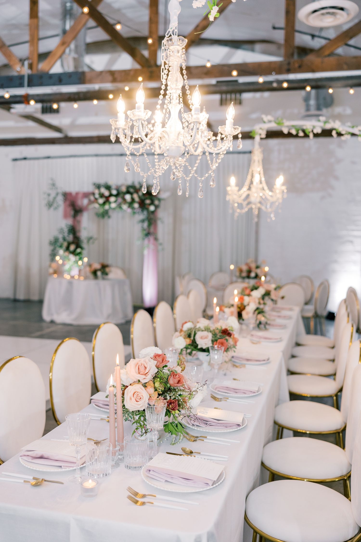 Elegant white wedding reception setup with crystal chandeliers and floral centerpieces.
