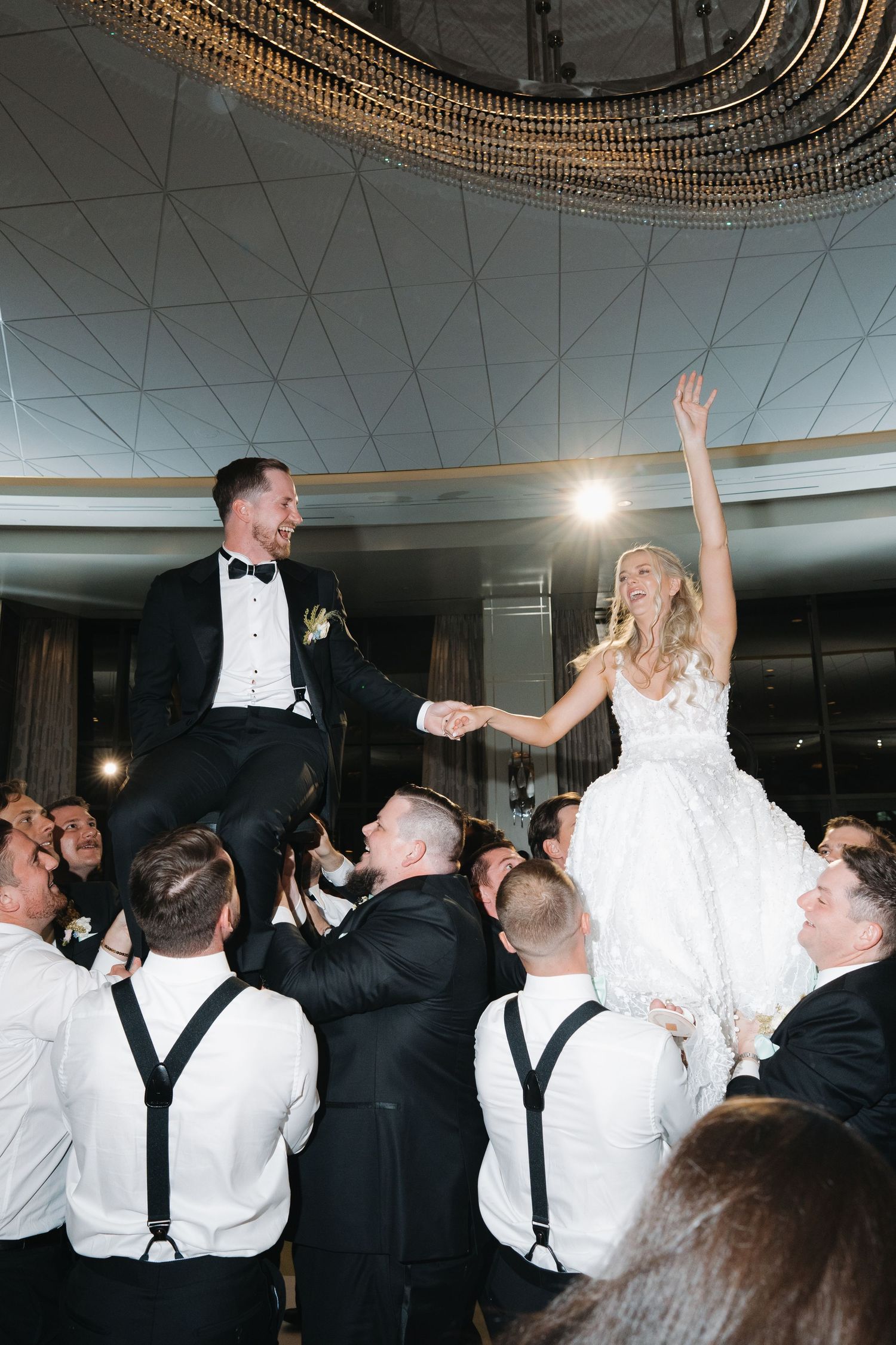 Bride and groom are lifted by groomsmen during lively hora dance at wedding reception celebration.
