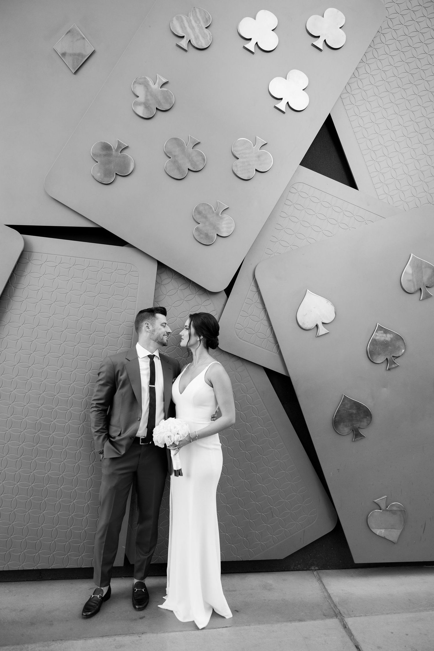 Black and white photo of a bride and groom kissing in front of a giant playing card wall mural in Las Vegas.