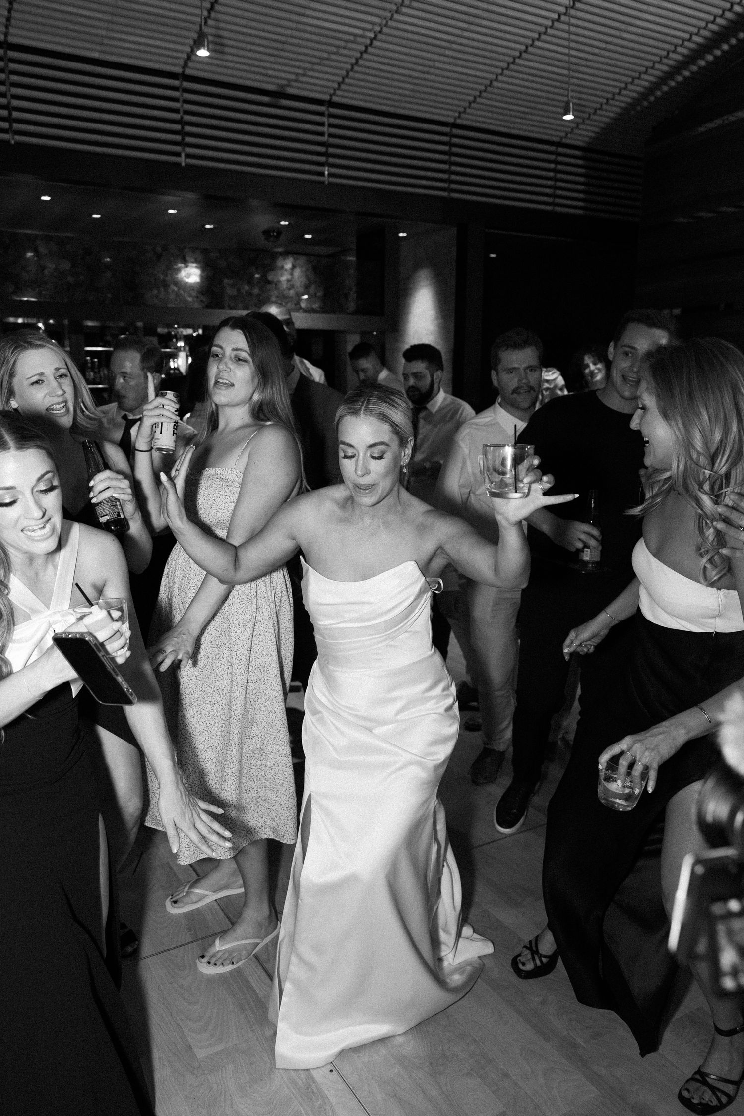 Bride in strapless white gown dances with wedding guests at lively black and white reception party.