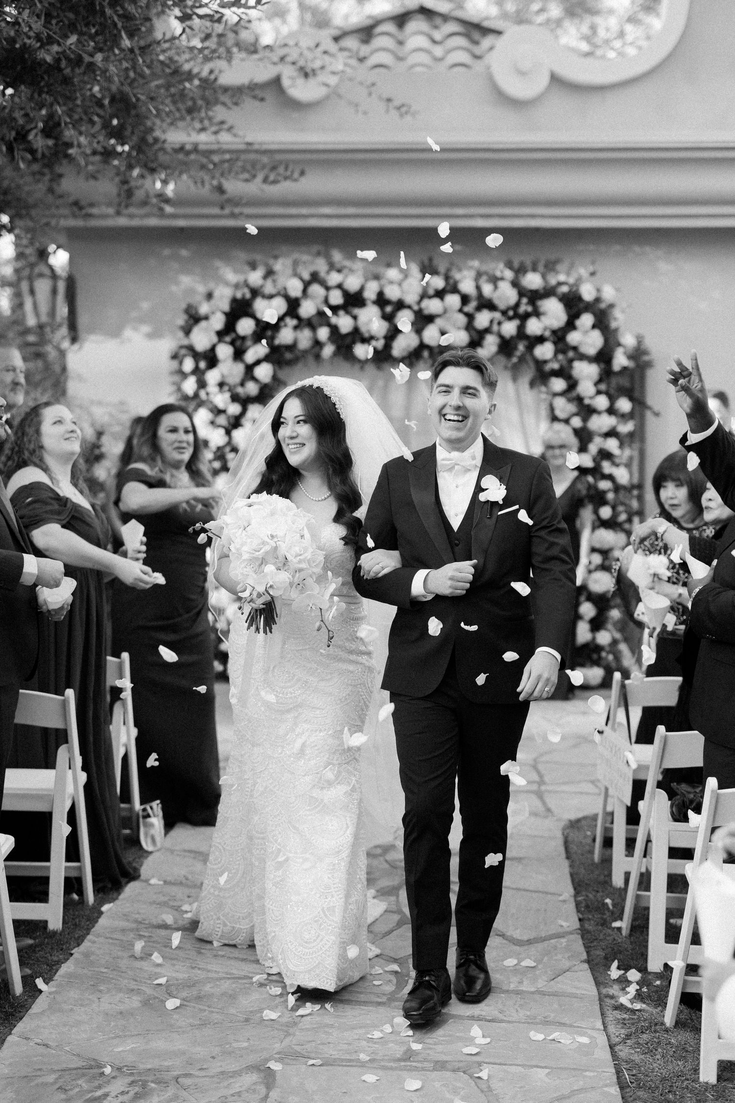 A joyful wedding ceremony recessional with the couple walking down the aisle as guests throw white flower petals in celebration.