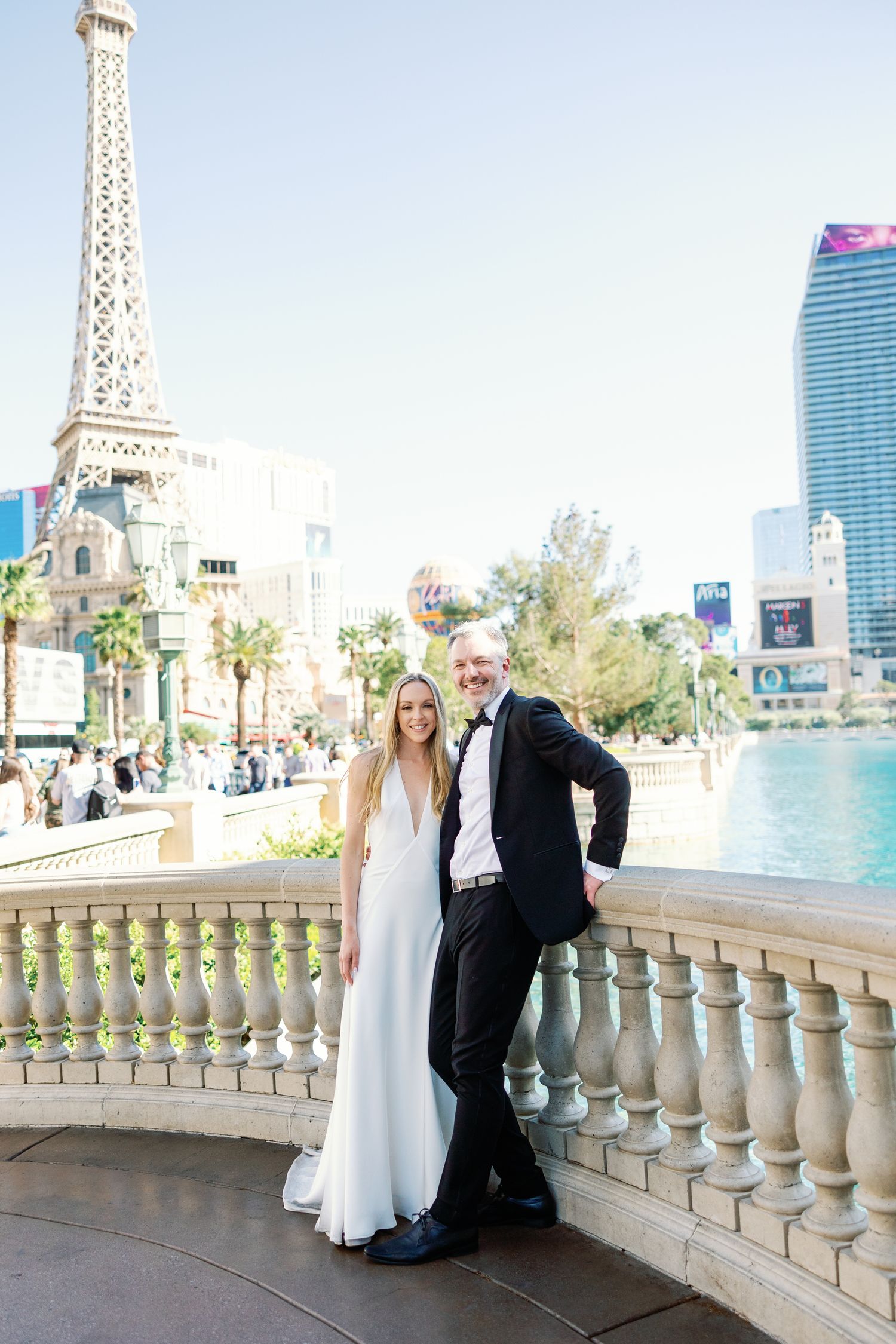 A bride and groom pose near the Bellagio fountains with the Paris Las Vegas Eiffel Tower replica in the background.